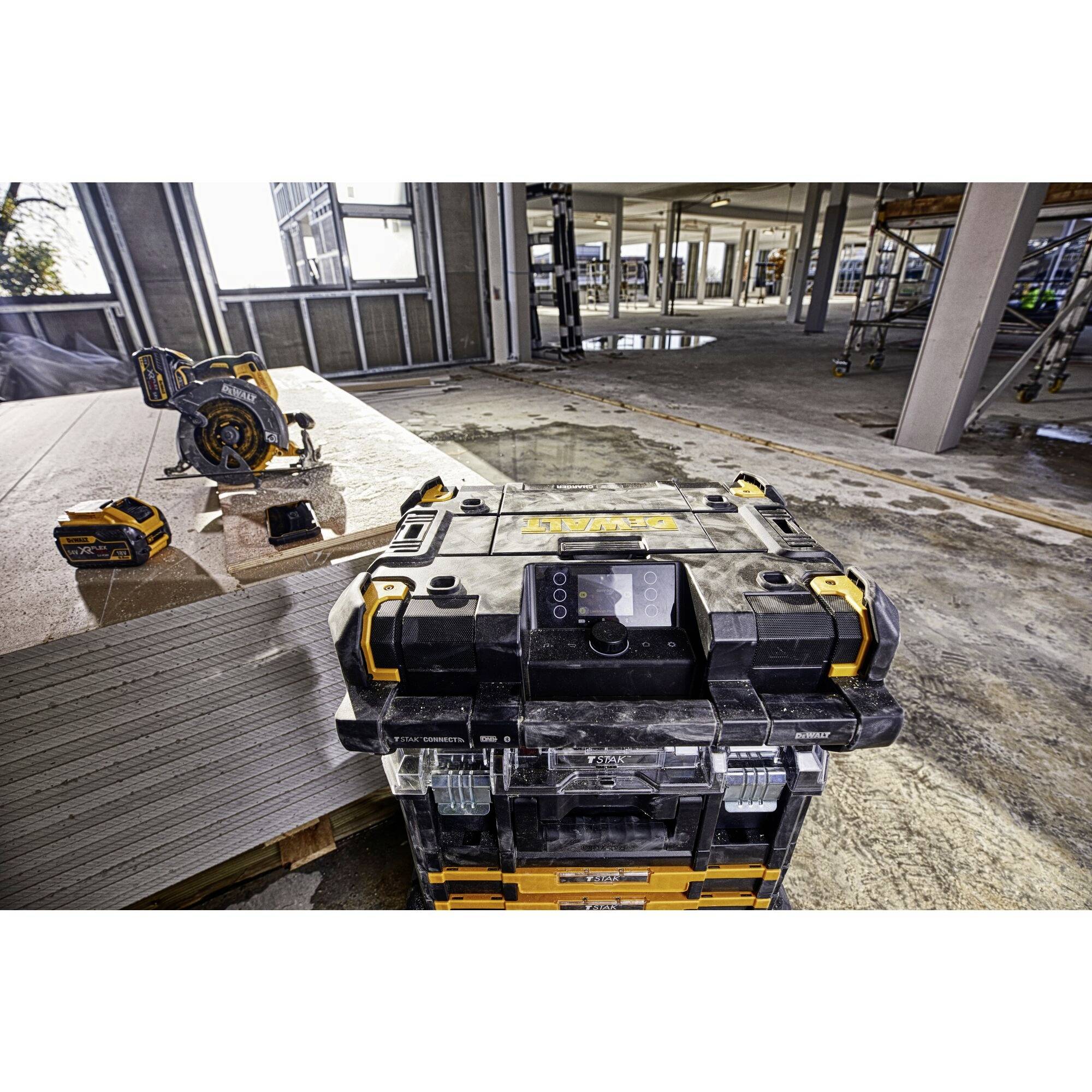 Un cantiere con diversi dispositivi elettrici, tra cui un contenitore degli attrezzi portatile, una sega a batteria e un capannone vuoto sullo sfondo.