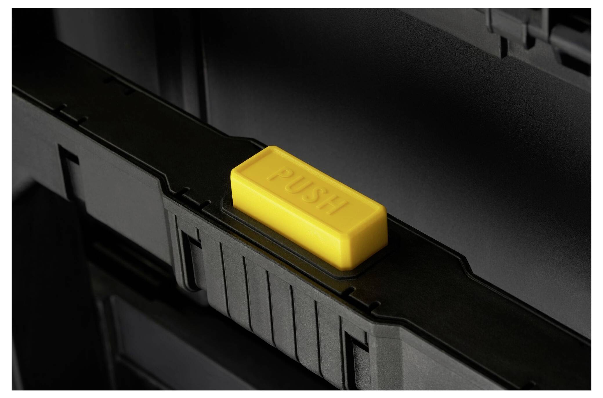 Un pulsante giallo con la scritta 'PUSH' su una superficie di plastica nera, probabilmente parte di un meccanismo di chiusura.