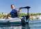 Persona su un gommone in un lago, indossa un giubbotto di salvataggio e tiene il timone di un motore elettrico. Sullo sfondo case residenziali.