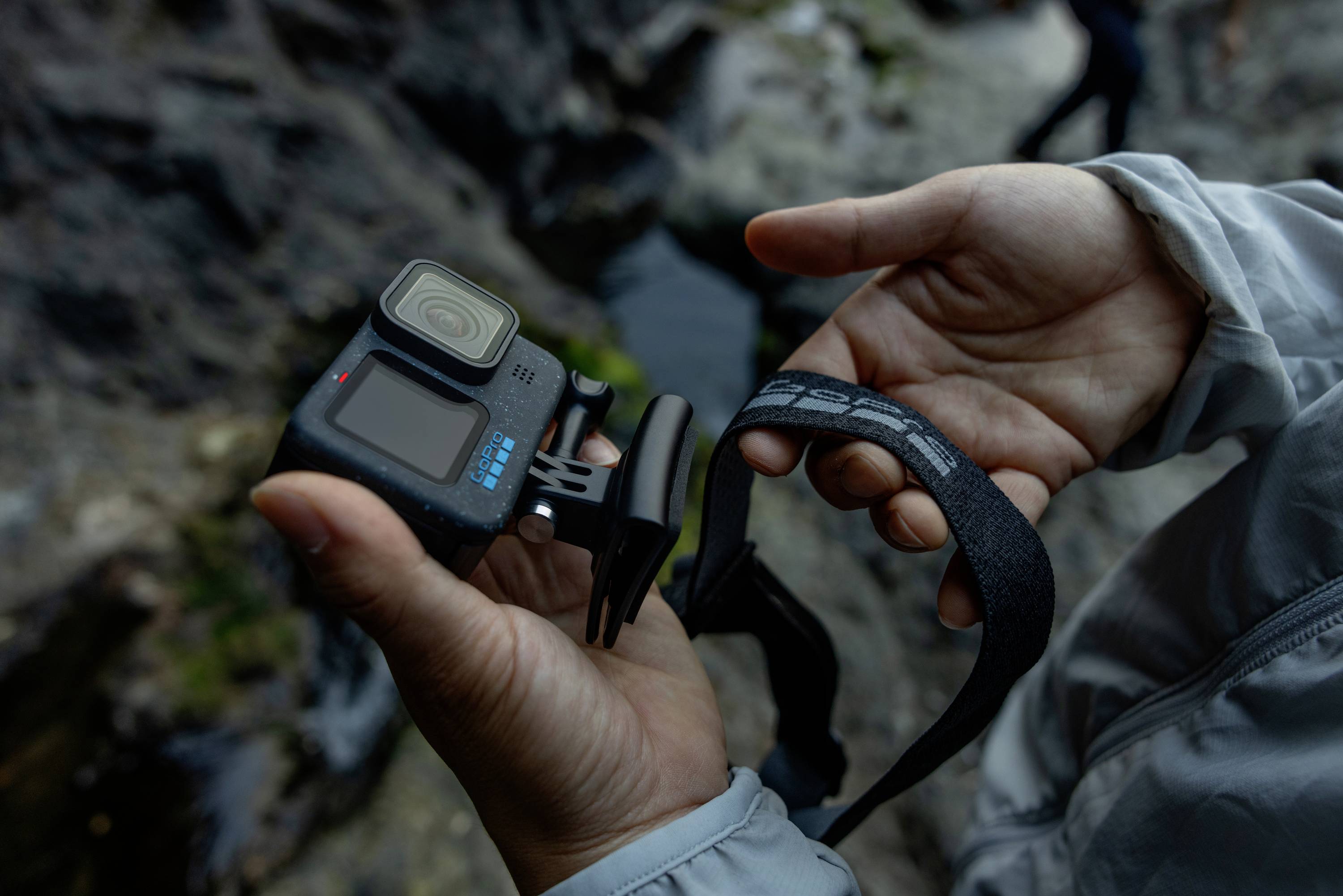 Una persona tiene in mano una fotocamera compatta per azione, pronta a riprendere un video o scattare una foto all'aperto. Sullo sfondo, delle rocce.