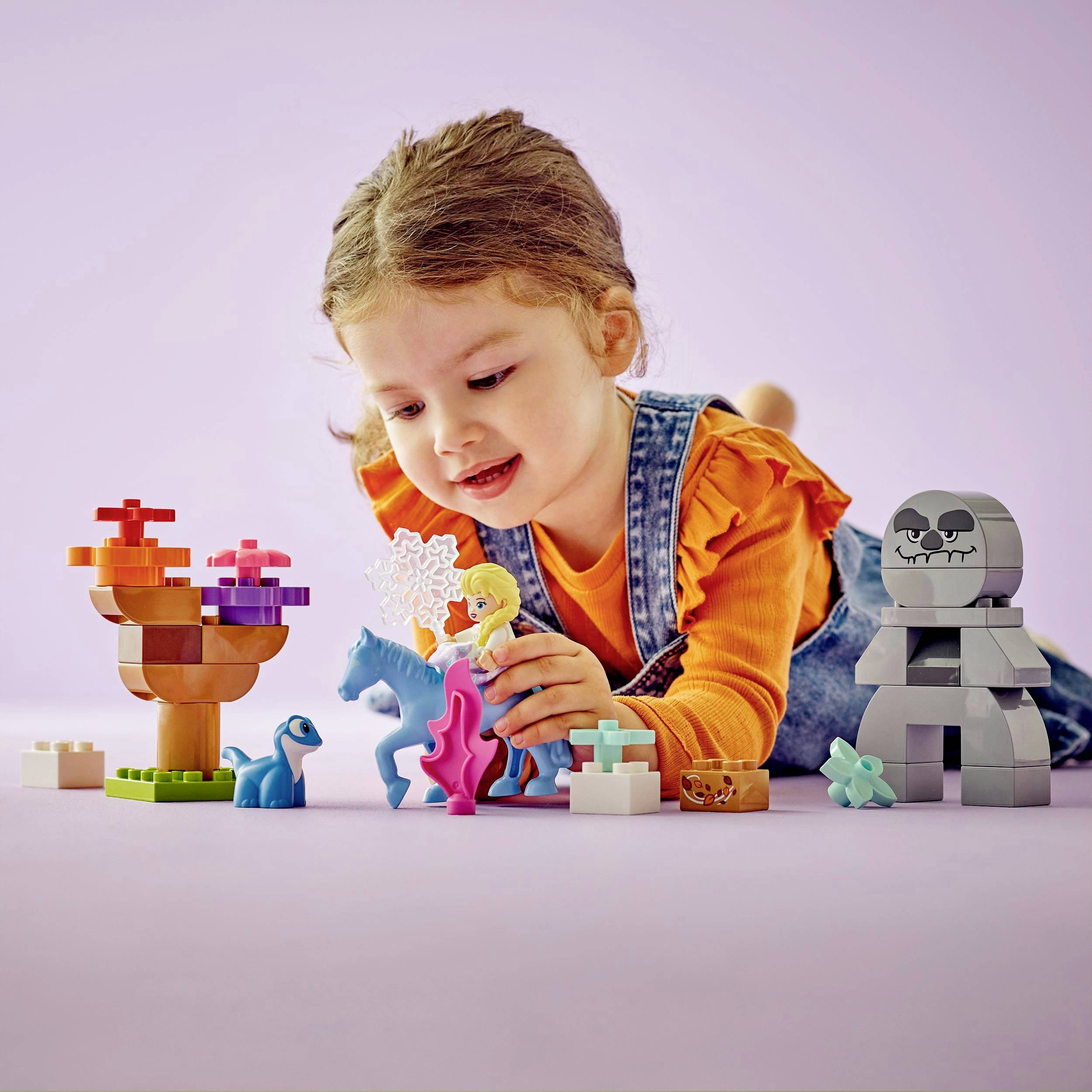 Un bambino gioca con figure di plastica colorate e blocchi sul pavimento. Le figure includono un unicorno, un dinosauro e altre creature fantastiche.