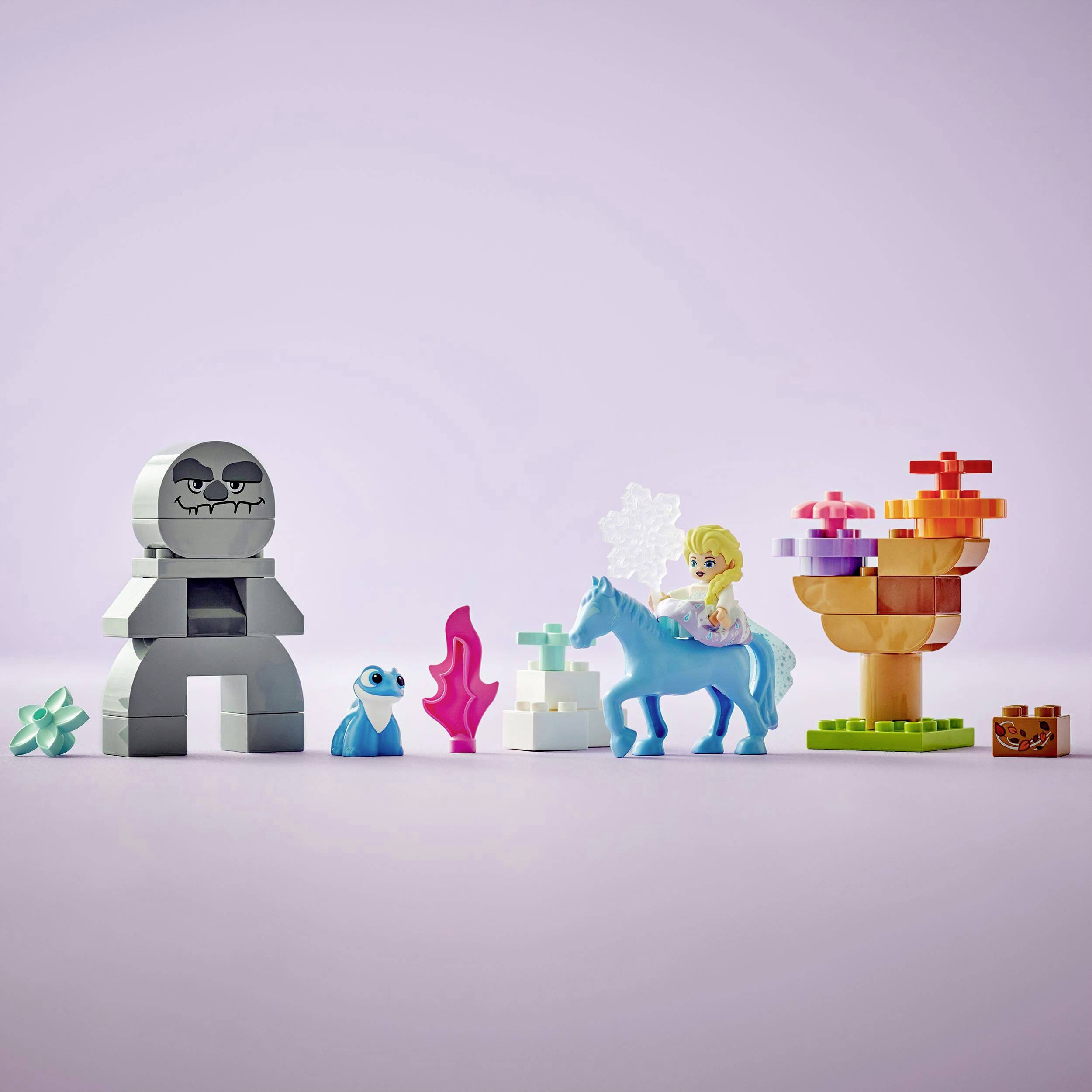 Una scena Lego mostra figure e oggetti colorati, tra cui un robot, un animale blu, una statuetta su un cavallo e delle piante.