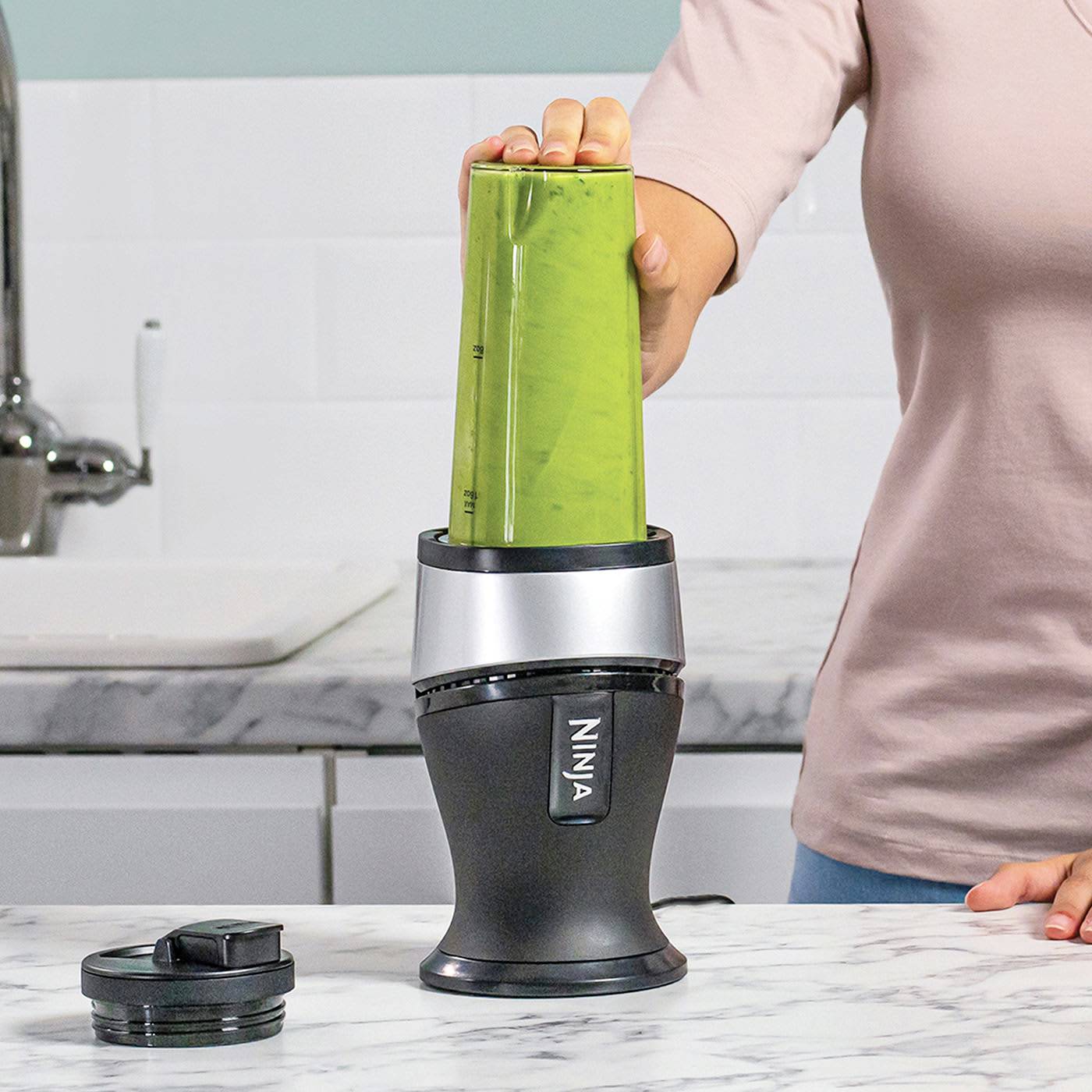 Una persona sta usando un frullatore per preparare uno smoothie verde. Il frullatore è posizionato su un piano da cucina, e non sono visibili altri ingredienti.
