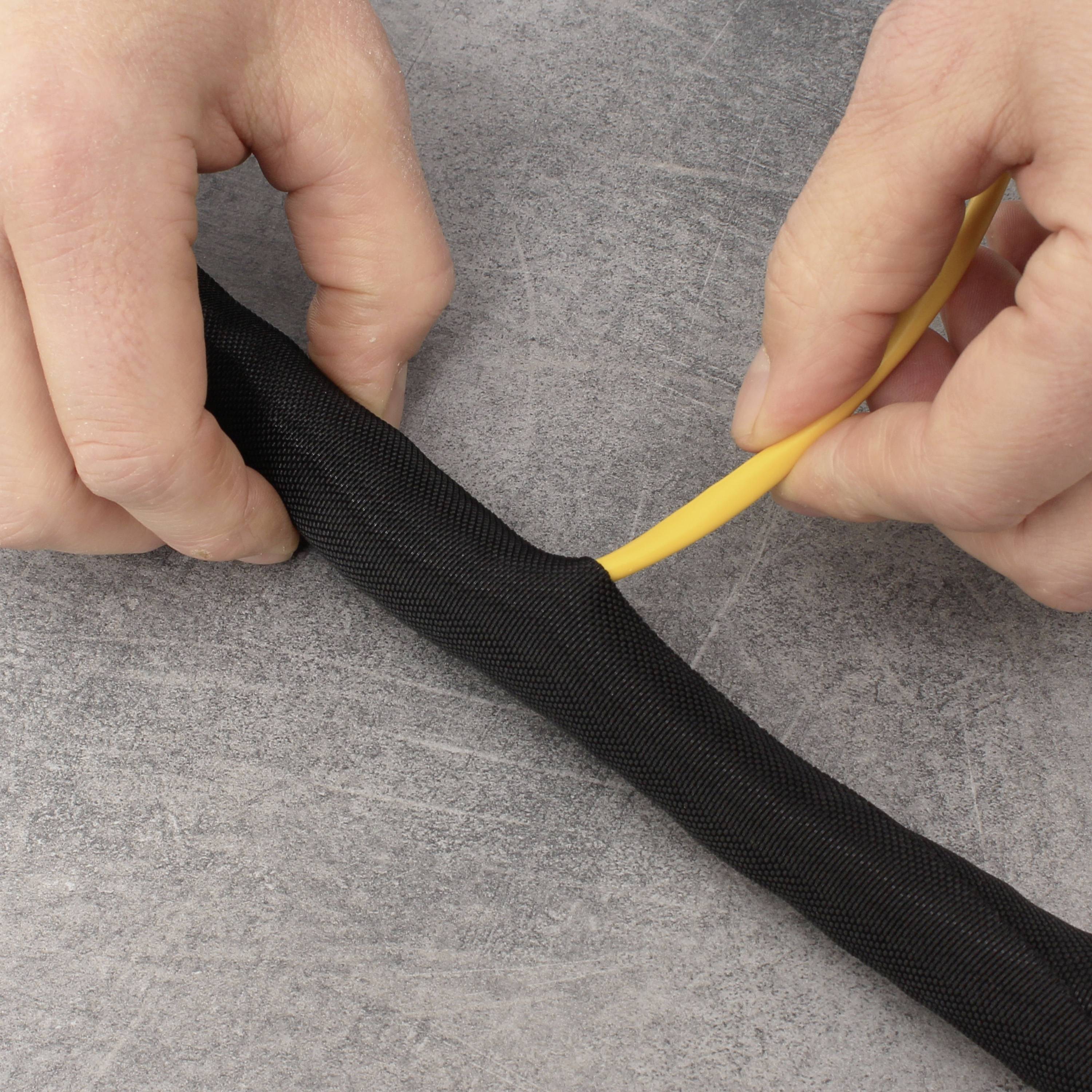 Due mani inseriscono un cavo giallo attraverso una guaina protettiva nera su una superficie grigia.