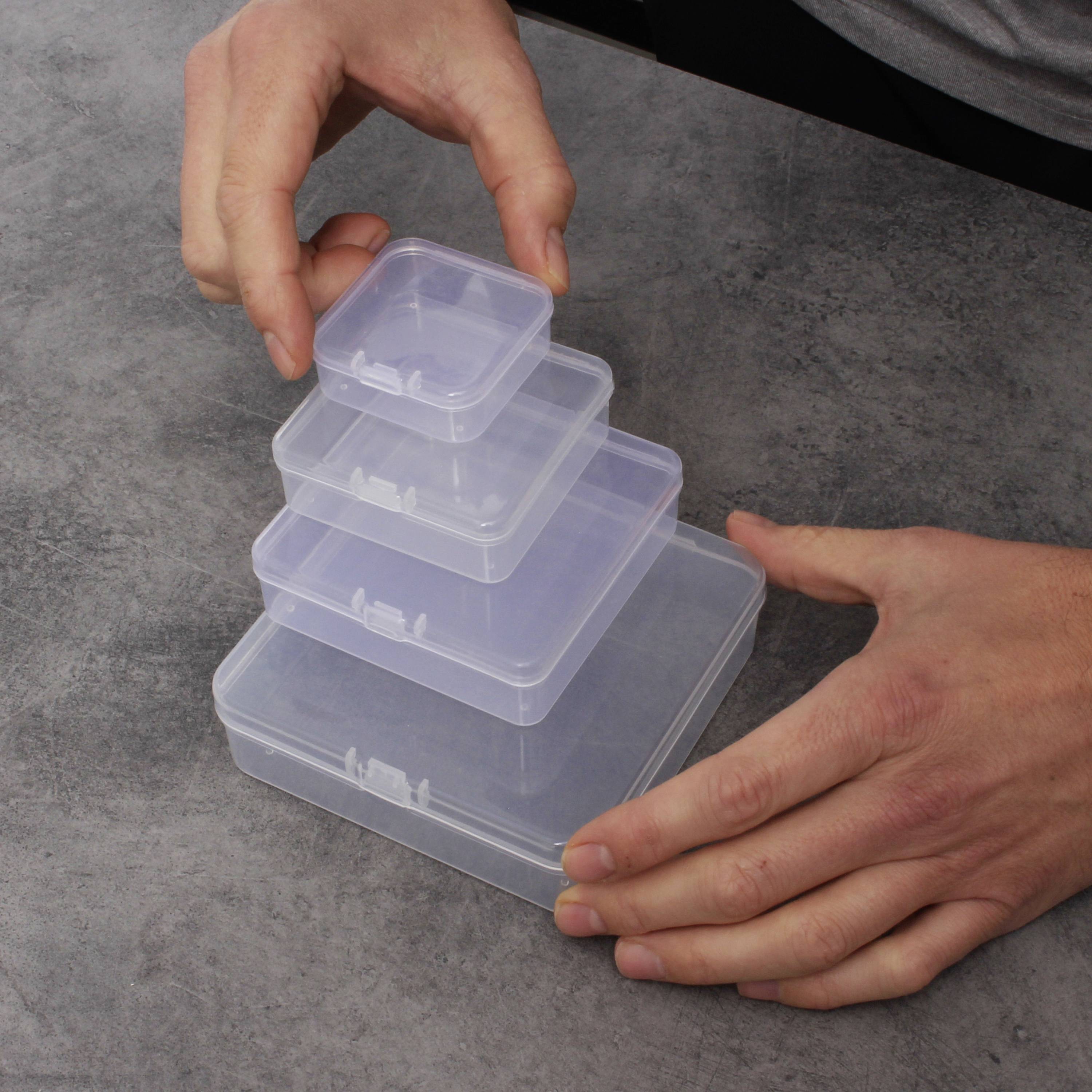 Le mani di una persona impilano quattro scatole di plastica trasparenti di dimensioni decrescenti su un tavolo grigio.