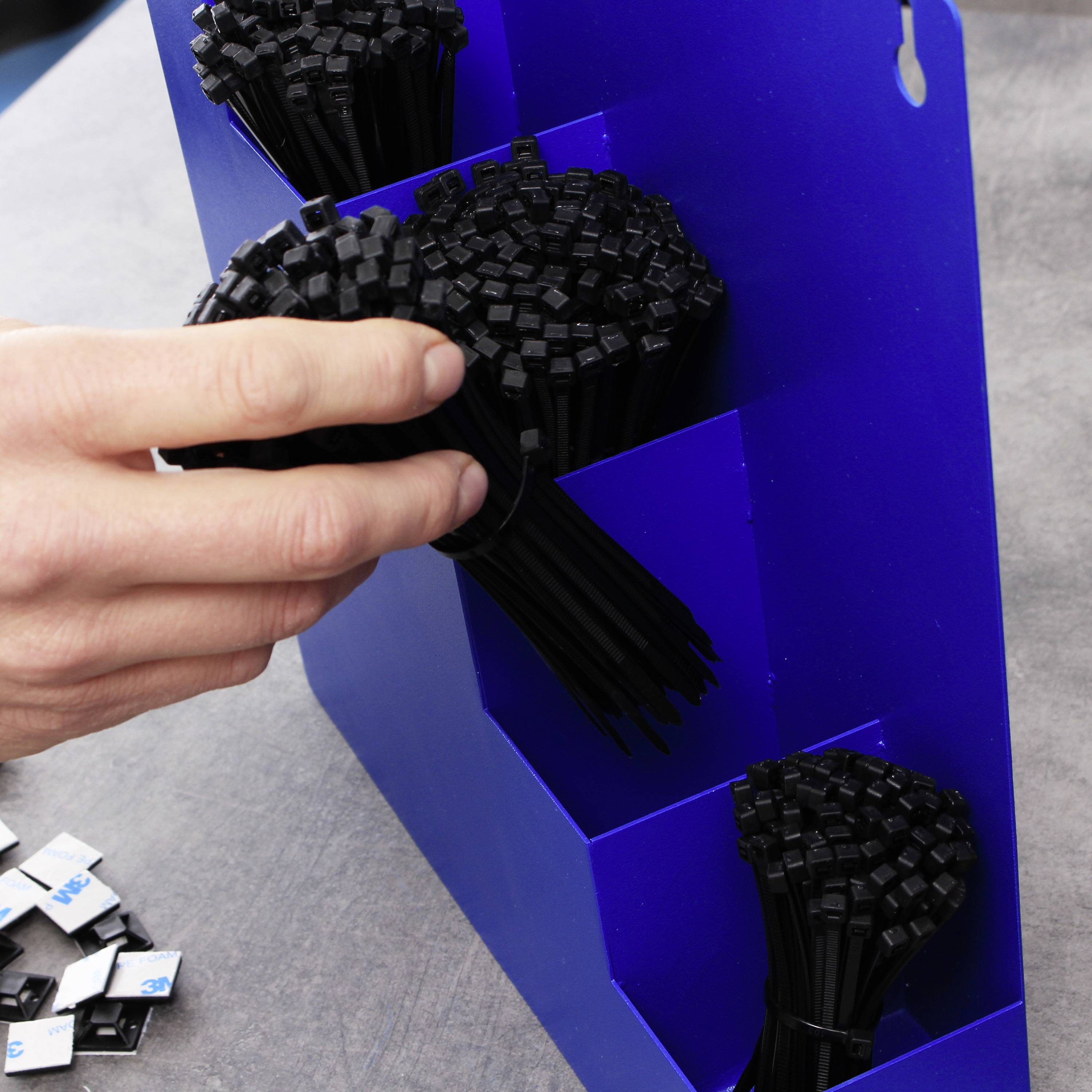 Una persona afferra un mazzo di fascette per cavi nere in un supporto blu, circondato da piccoli pezzi di metallo su un tavolo.