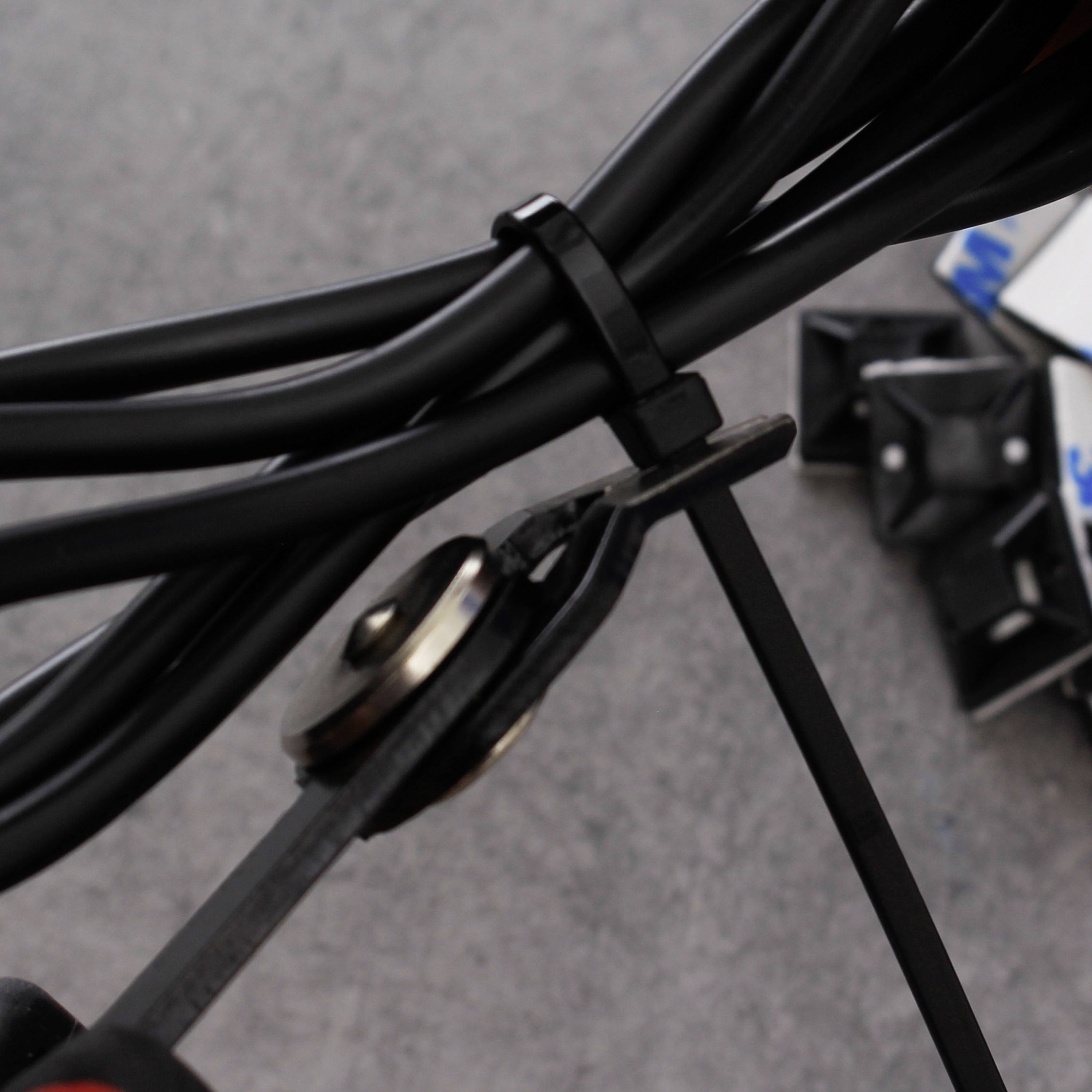 Una pinza taglia un cavo nero su uno sfondo grigio. Sullo sfondo, fascette per cavi sono sparse su un tavolo.