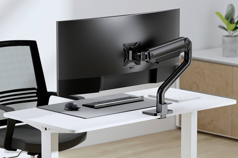 Un posto di lavoro moderno con un monitor curvo su un braccio snodabile, una tastiera, un mouse su un tavolo bianco. Una sedia da ufficio è posizionata accanto.