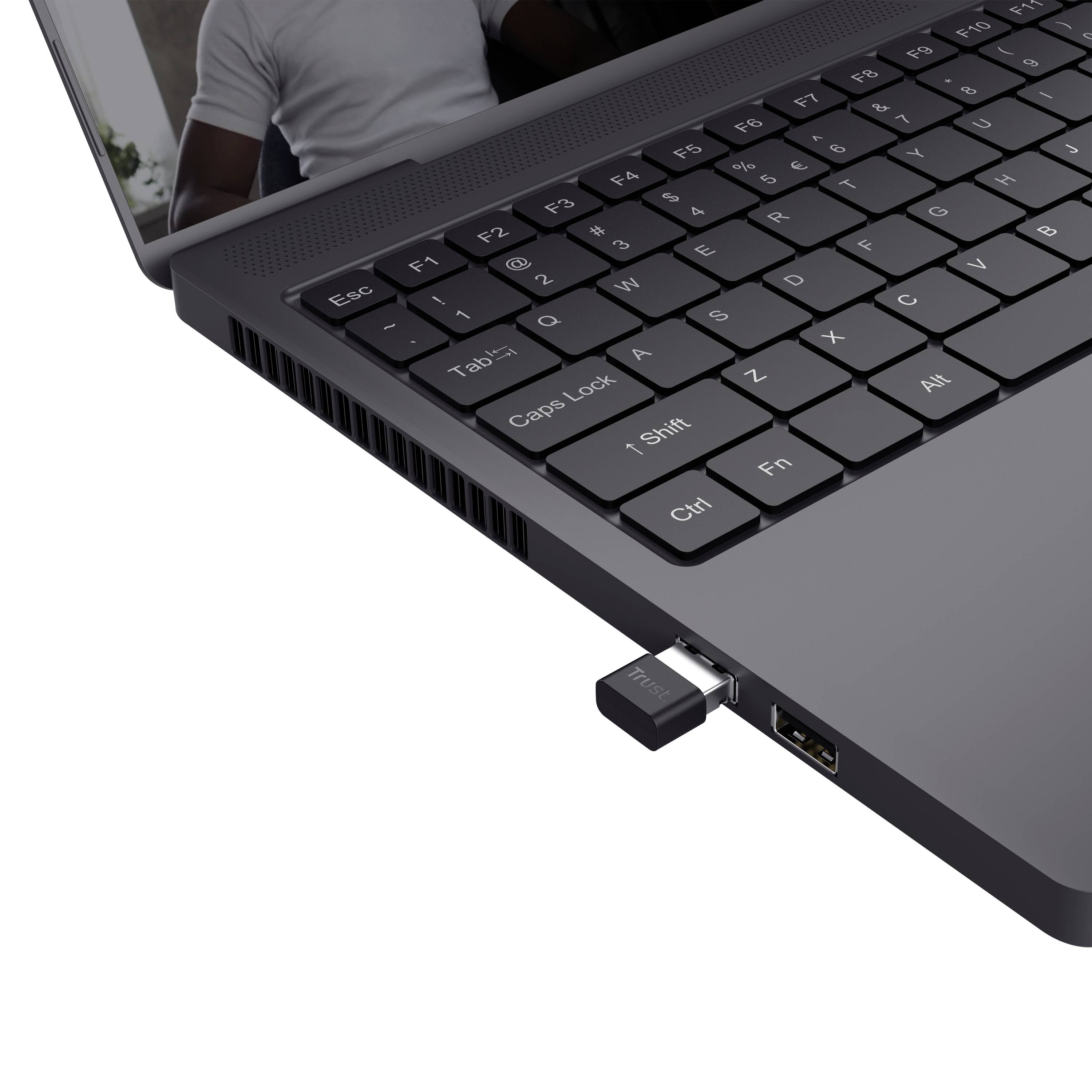 Un laptop nero con una tastiera USB, collegata tramite una porta USB sul lato destro. Sullo sfondo si vedono persone sfocate.