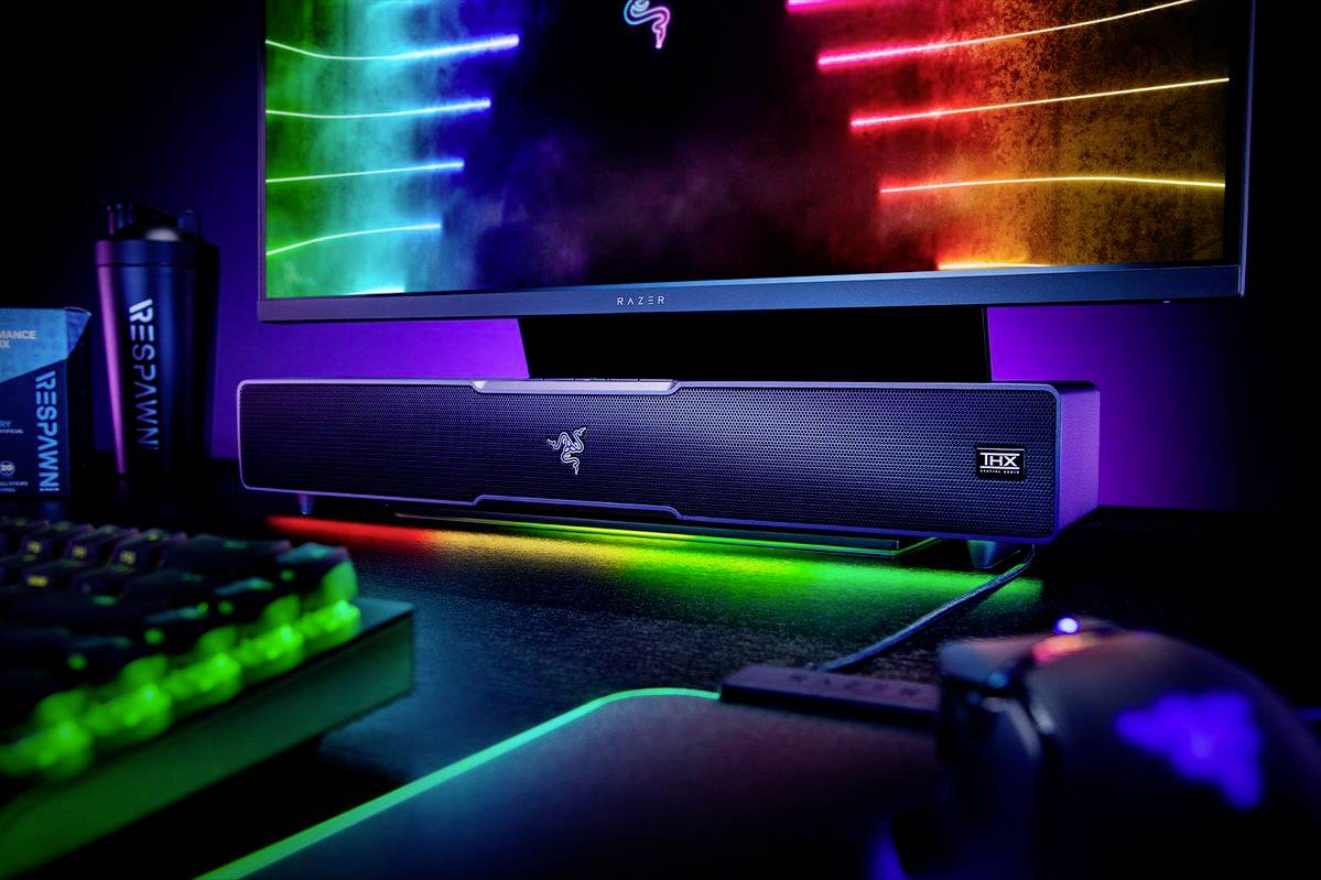 Postazione da gaming con monitor illuminato, soundbar e tastiera in colori RGB. I colori al neon creano un'atmosfera futuristica.