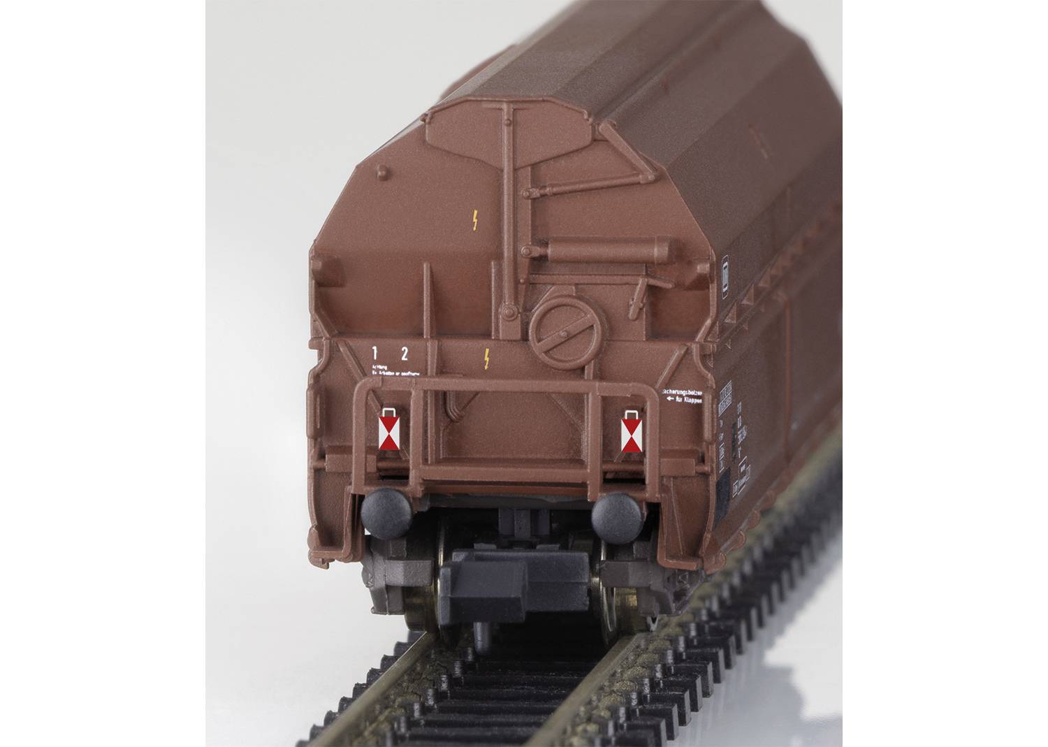 Un vagone merci per modellismo ferroviario sui binari, verniciato di marrone, con scritte bianche e marcature rosse.