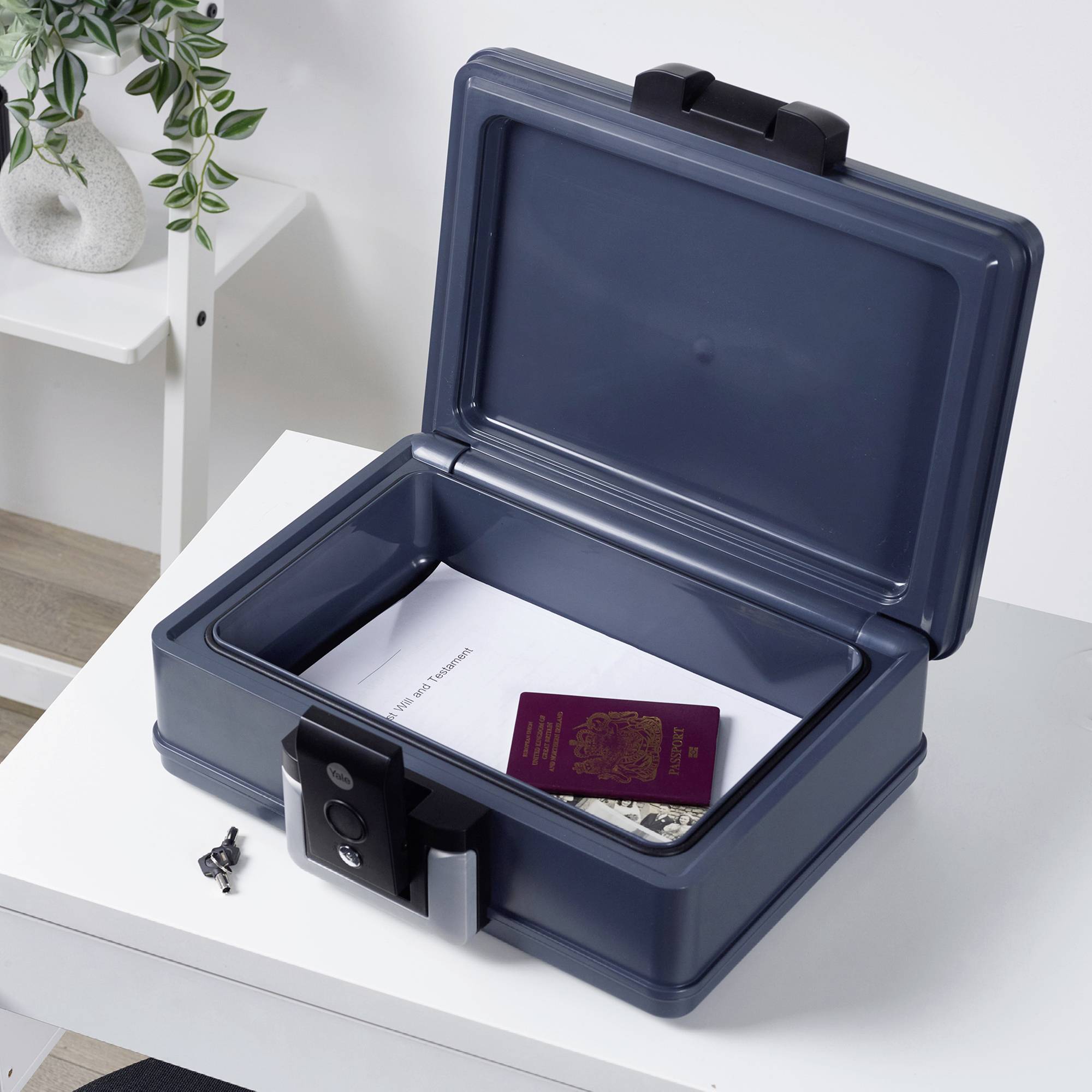 Un cassaforte aperto su un tavolo contiene un passaporto e dei documenti. La cassaforte è blu scuro e assicurata con un lucchetto.