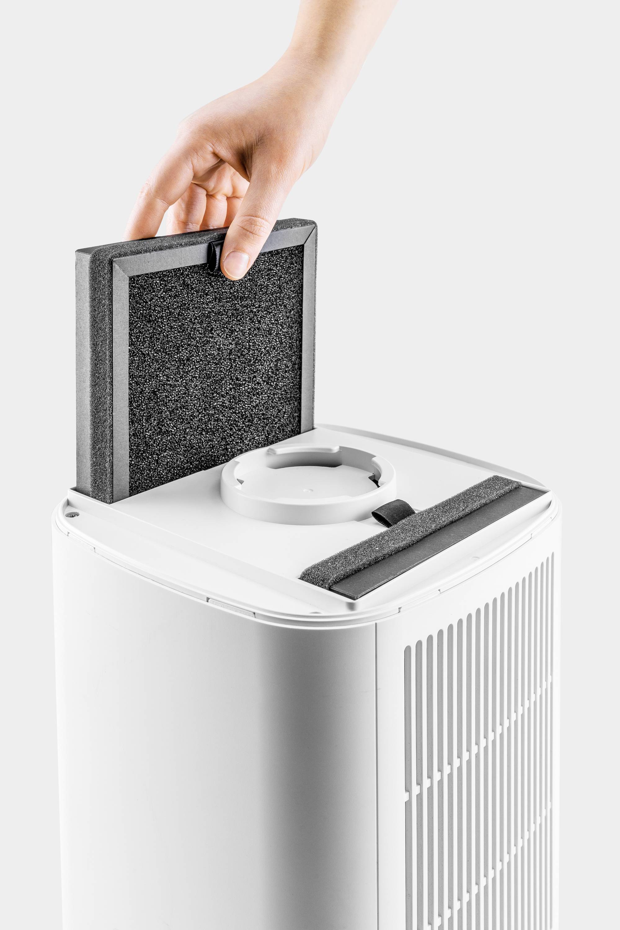 Una mano sta cambiando il filtro di un purificatore d'aria bianco. Il nuovo filtro rettangolare viene inserito nell'apparecchio.