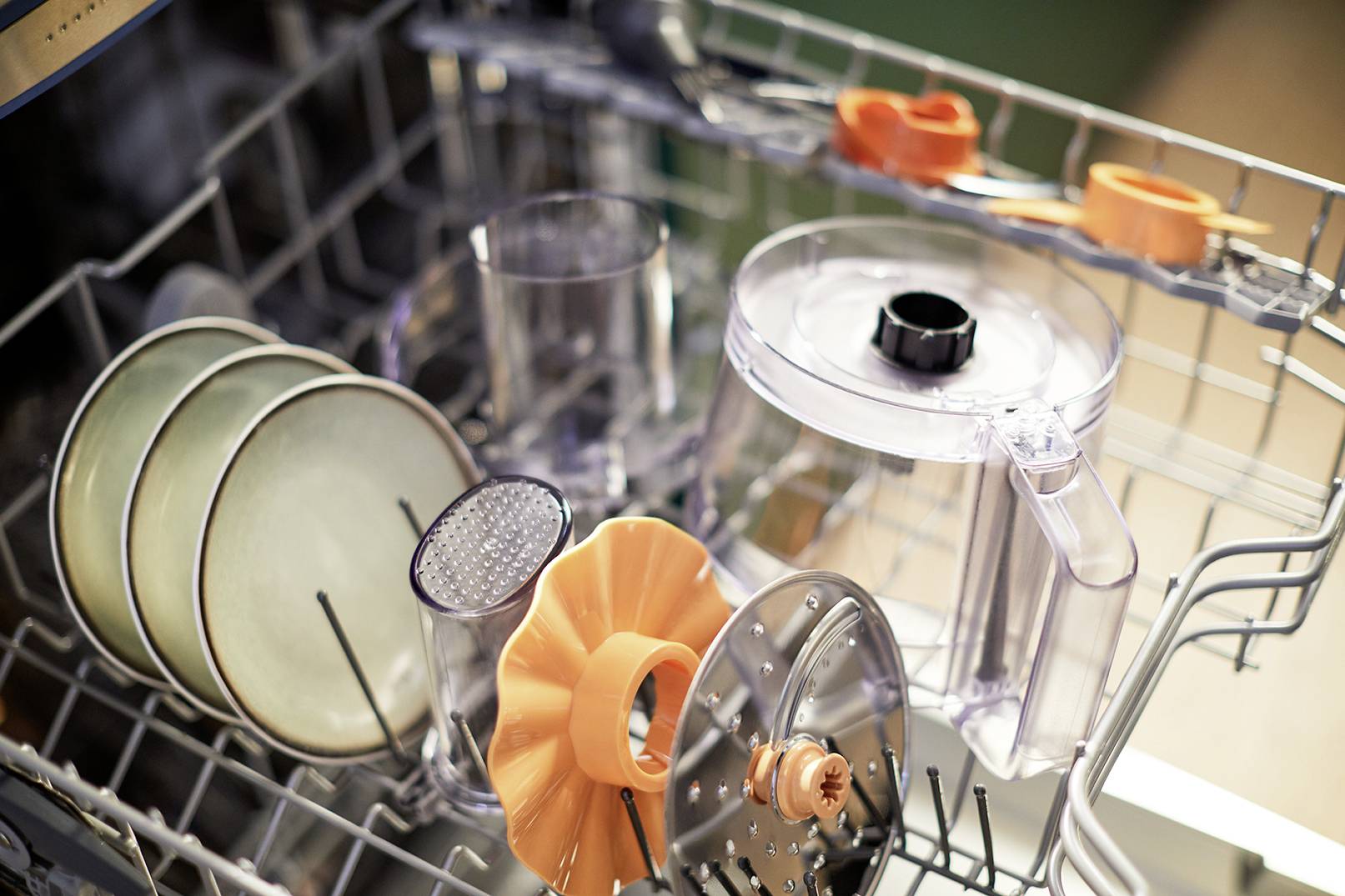 Lavastoviglie con lo sportello aperto, contenente diversi utensili da cucina come piatti, accessori per frullatore e disco grattugia.