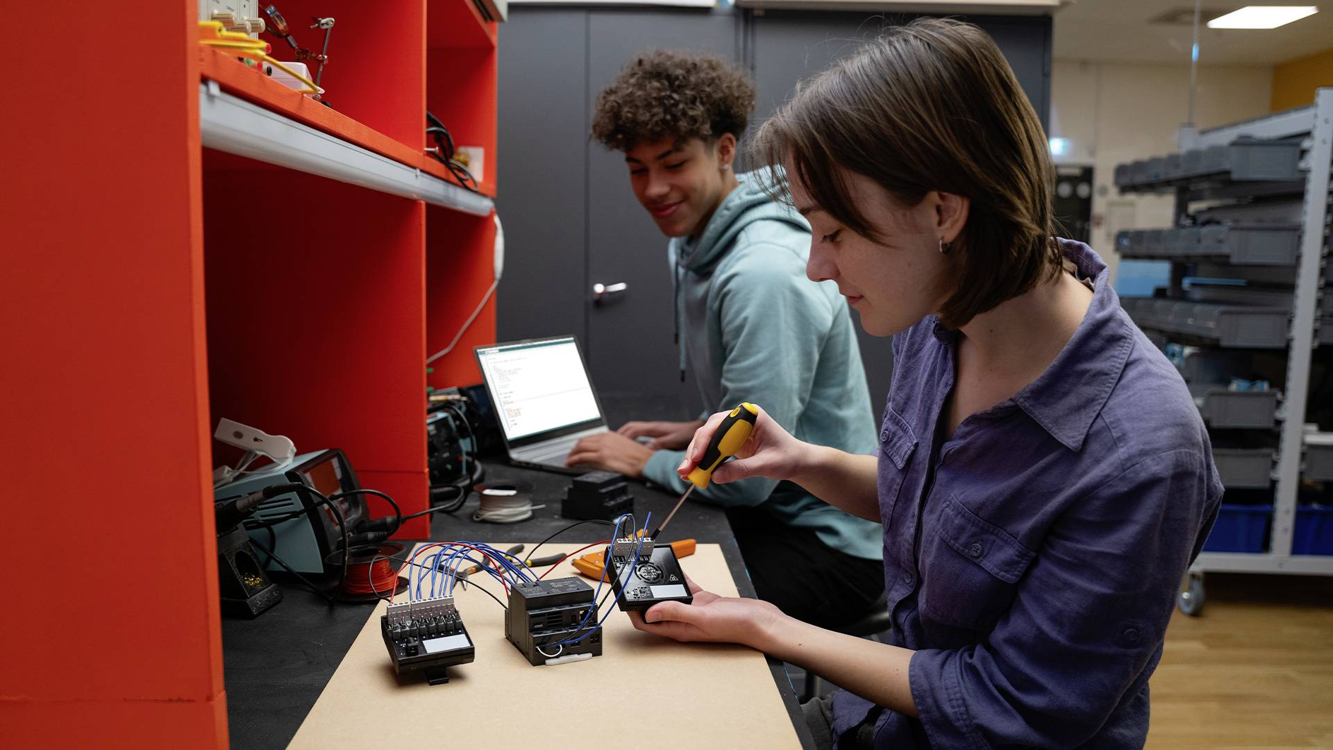 Due persone stanno lavorando a un progetto elettronico in un laboratorio. Una persona sta saldando, mentre l'altra sta lavorando sul laptop.