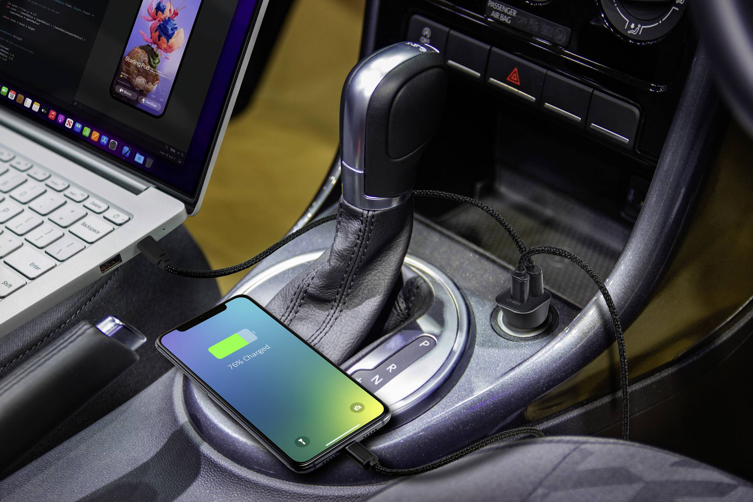 Un smartphone si sta caricando in auto, collegato tramite un cavo USB accanto a un laptop sulla console centrale.