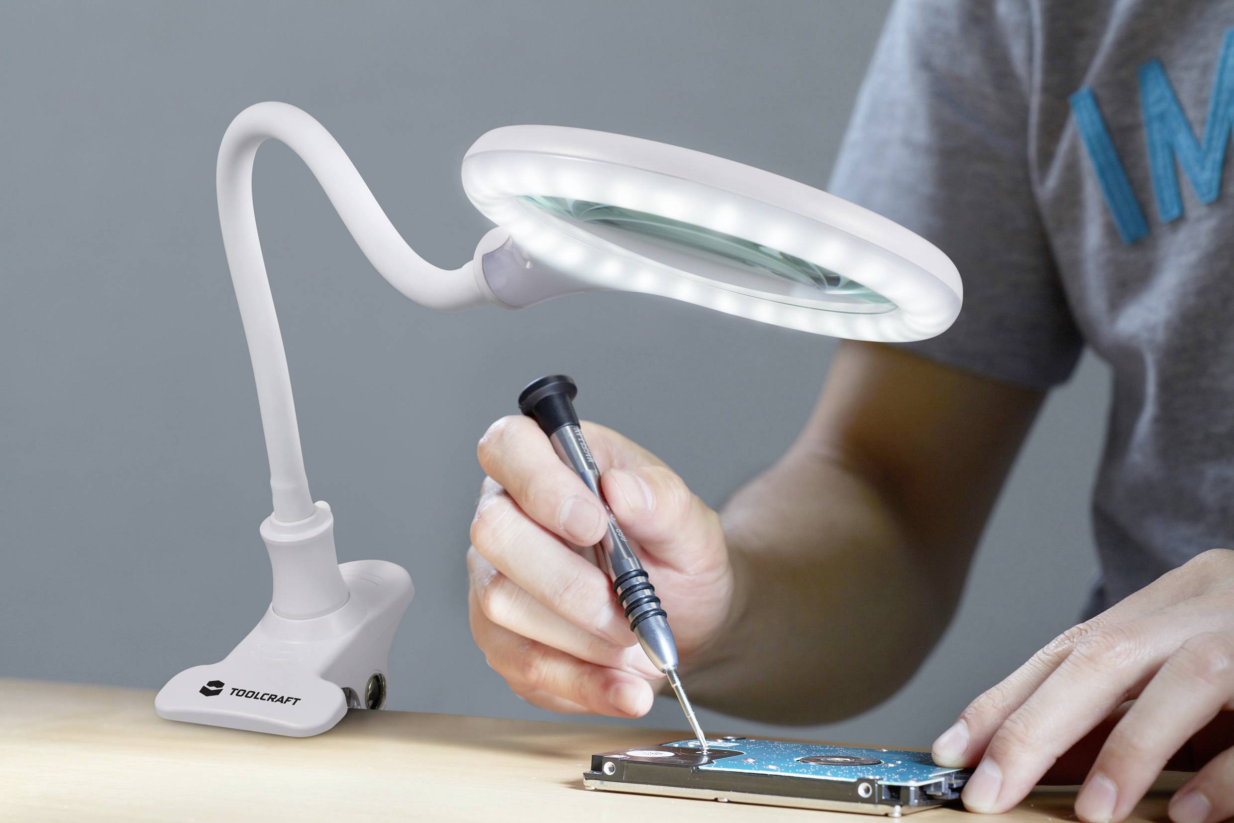 Una persona salda un dispositivo elettronico sotto una lente d'ingrandimento da tavolo con illuminazione a LED.