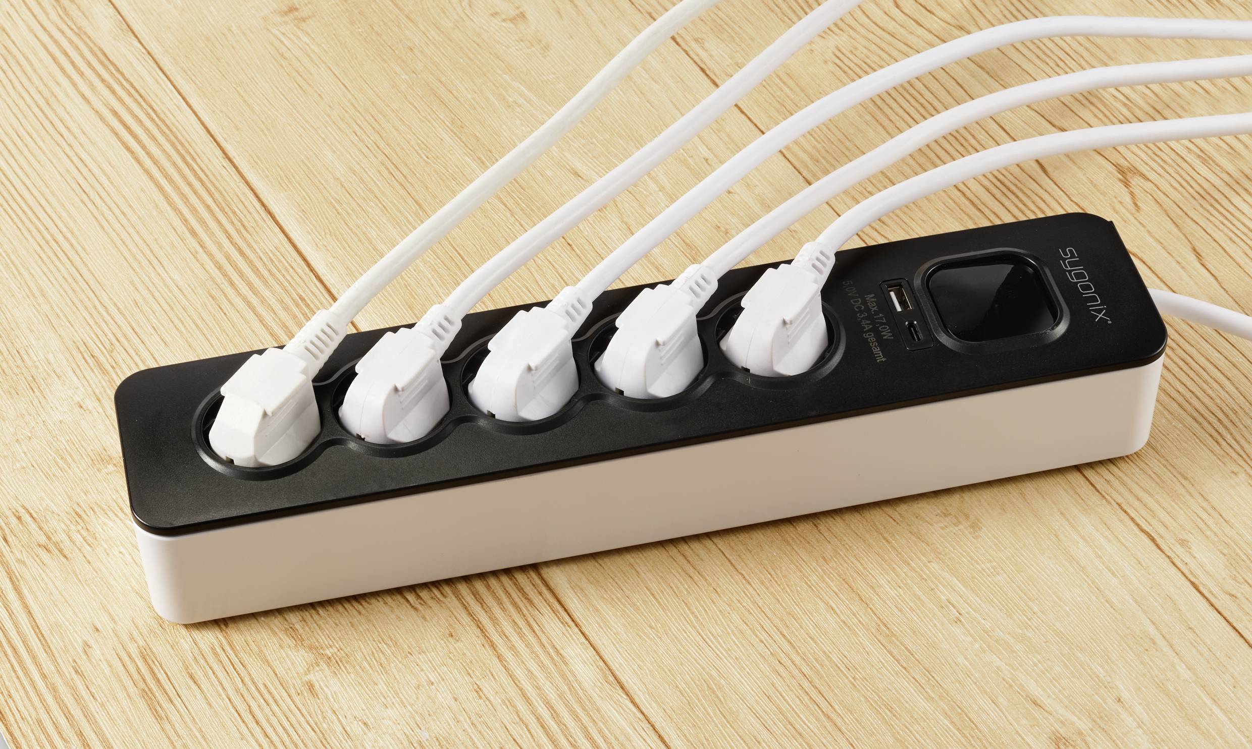 Una presa multipla nera su un tavolo di legno con cinque spine bianche inserite.