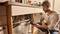 Un uomo è accovacciato davanti a un mobile della cucina aperto, tiene in mano uno smartphone e controlla i tubi sotto il lavandino; un secchio è pronto nelle vicinanze.