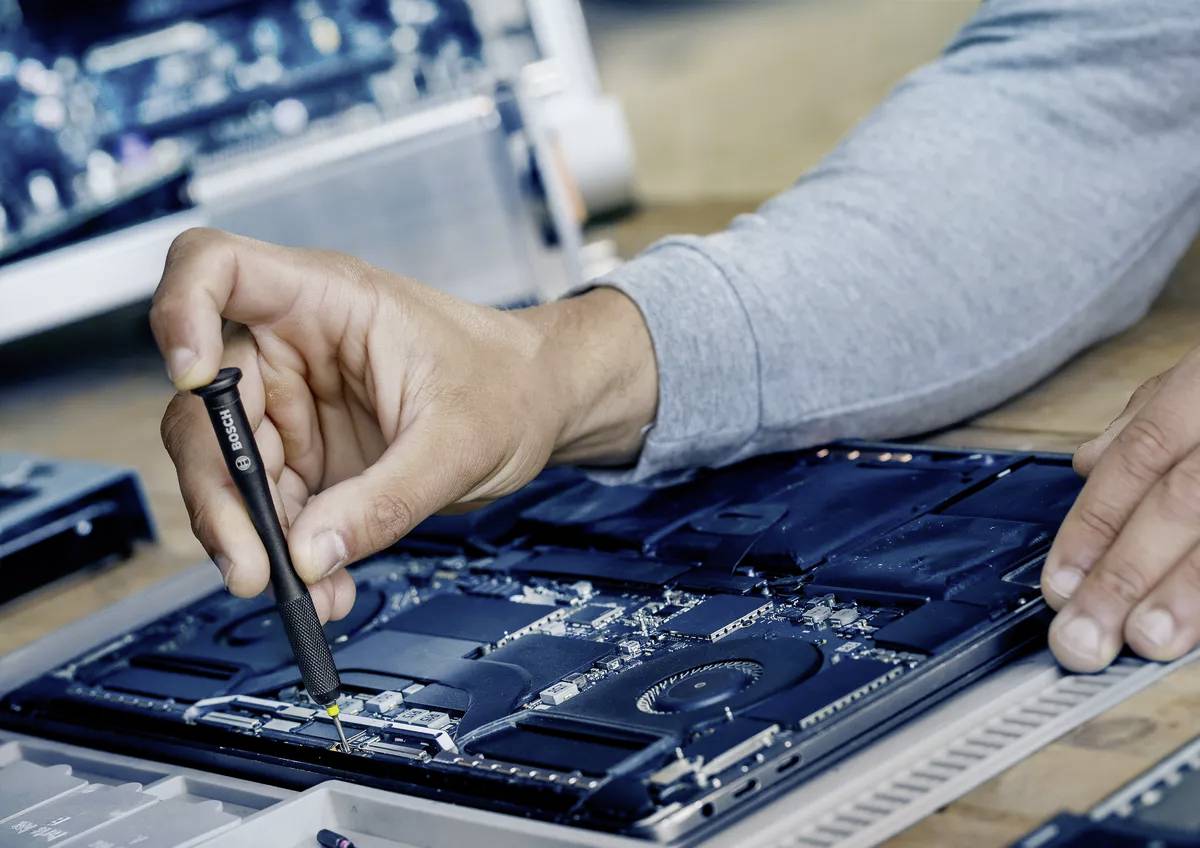 Una persona con un maglione grigio ripara un laptop aperto utilizzando un cacciavite, dimostrando competenza tecnica e precisione.
