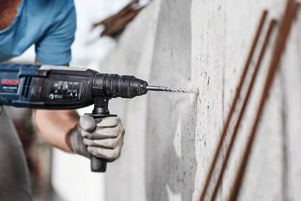 Una persona sta facendo un foro in un muro di cemento utilizzando un trapano elettrico, indossando guanti da lavoro.