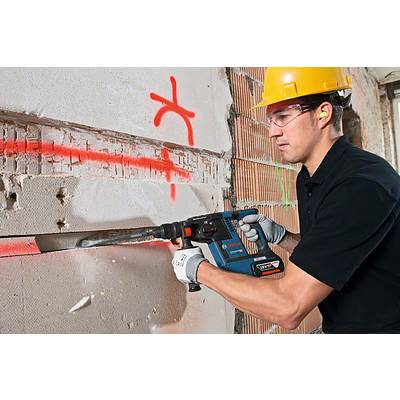 Un lavoratore edile con indumenti protettivi usa un martello pneumatico per abbattere un muro. Segni rossi sono visibili sul muro.
