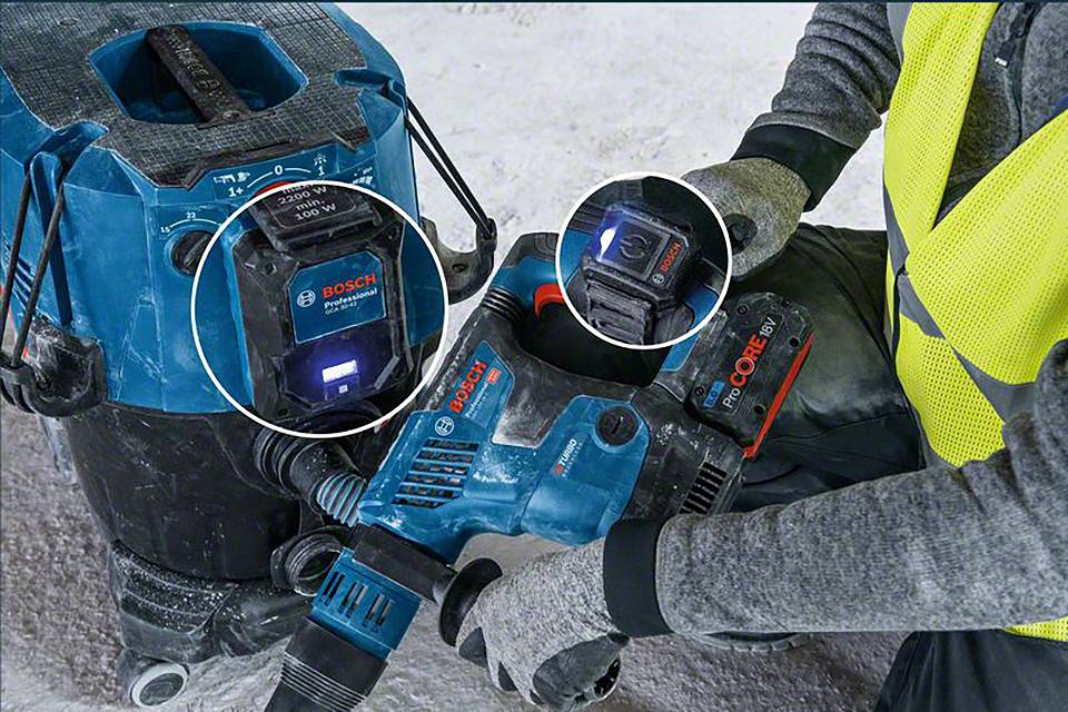 Una persona sta utilizzando un utensile elettrico Bosch con la relativa batteria, mentre un aspirapolvere è posizionato accanto.