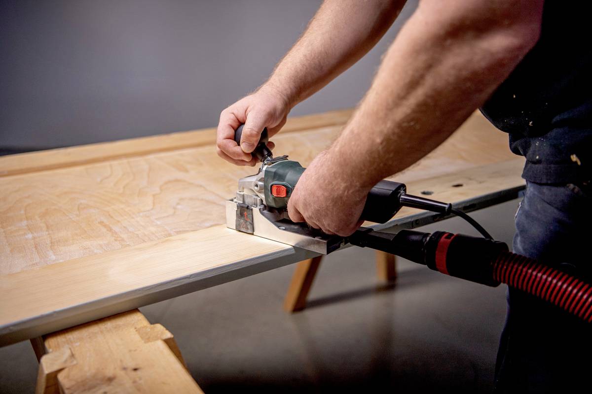 Una persona sta lavorando con una fresatrice elettrica su un pezzo di legno fissato a una panchina da lavoro.