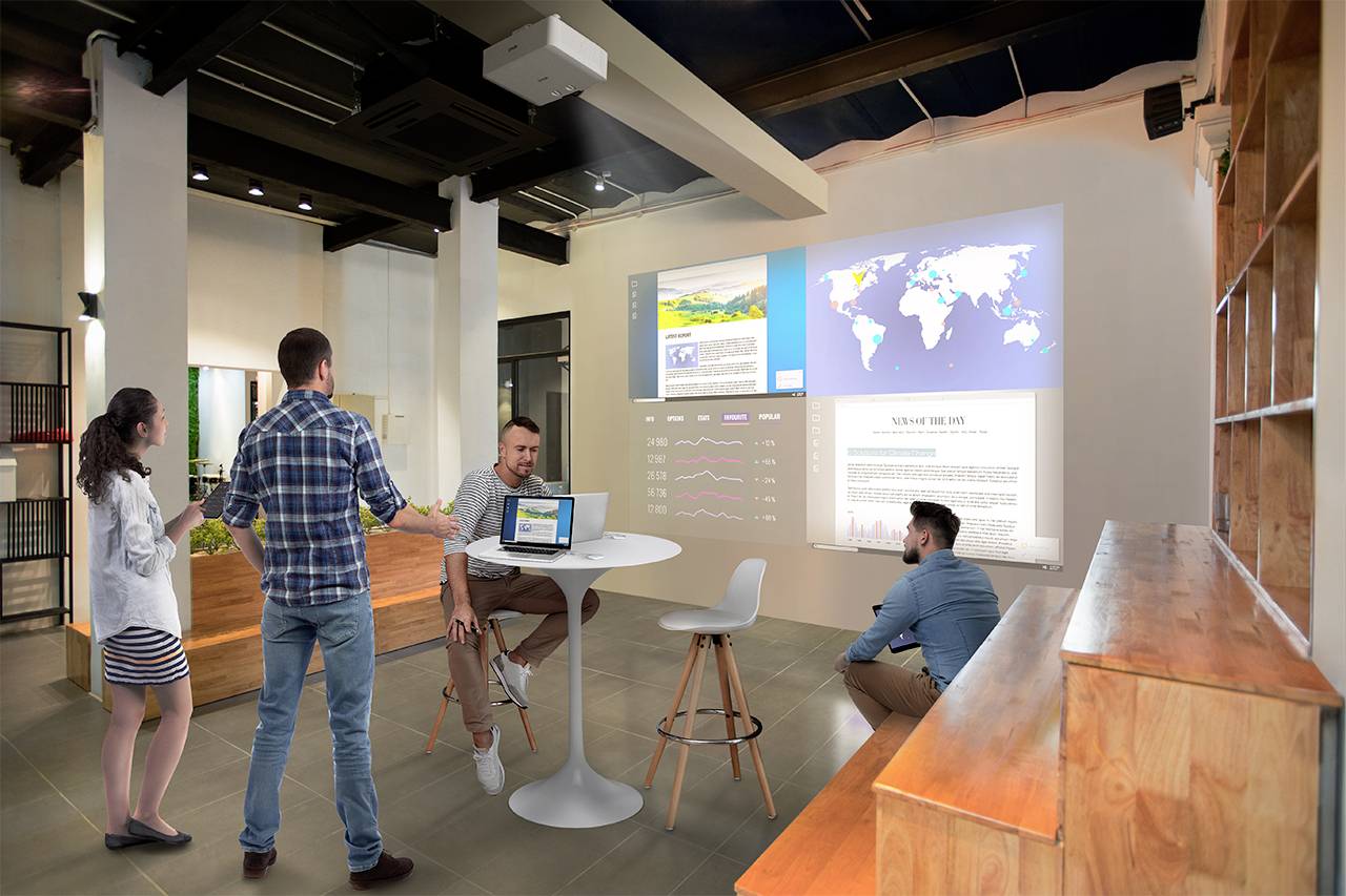 Un gruppo di persone sta discutendo in un ufficio moderno, mentre mappe e diagrammi vengono proiettati su una parete.