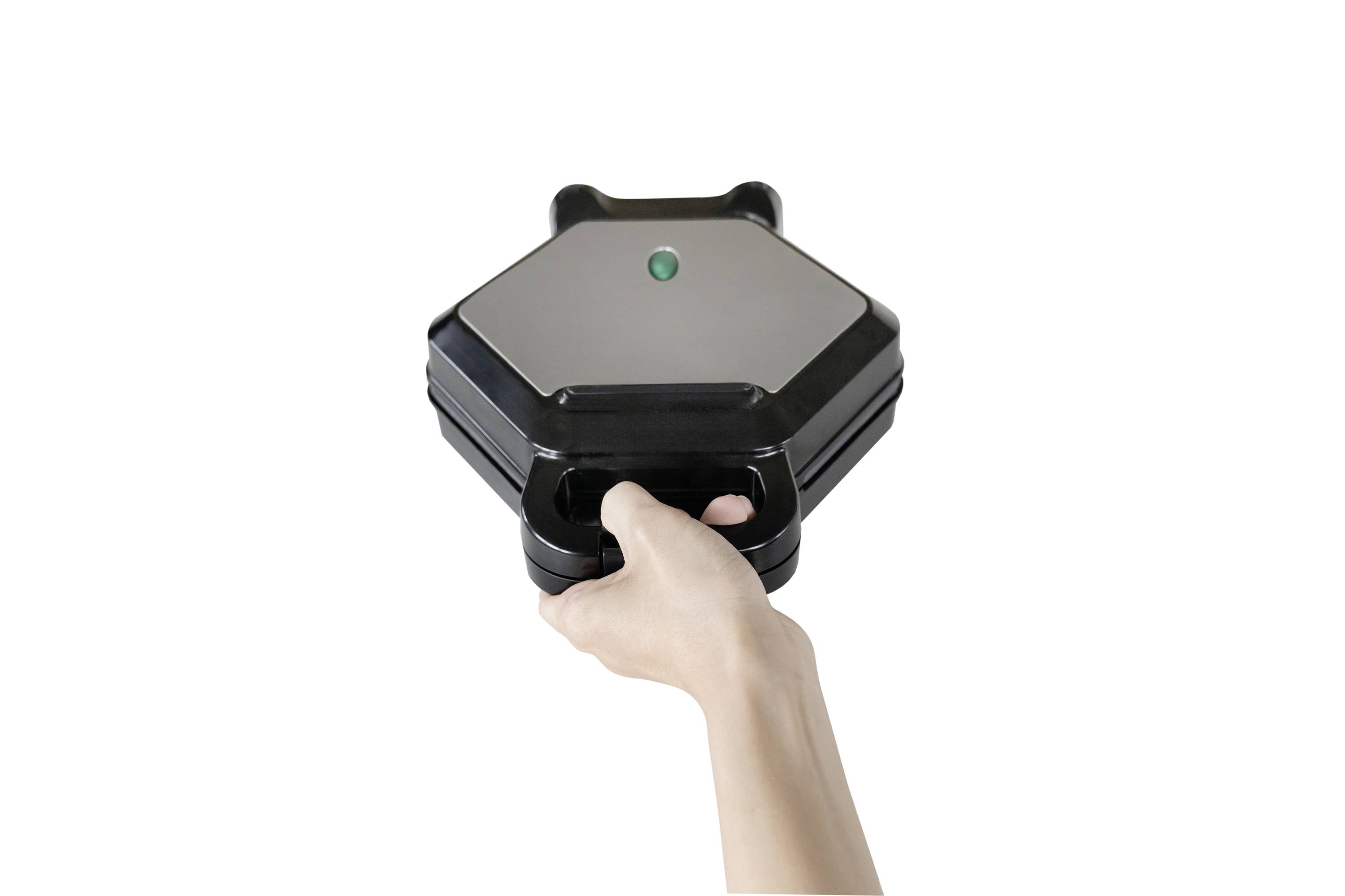 Una mano tiene un waffle maker nero esagonale con una luce verde sulla parte superiore.