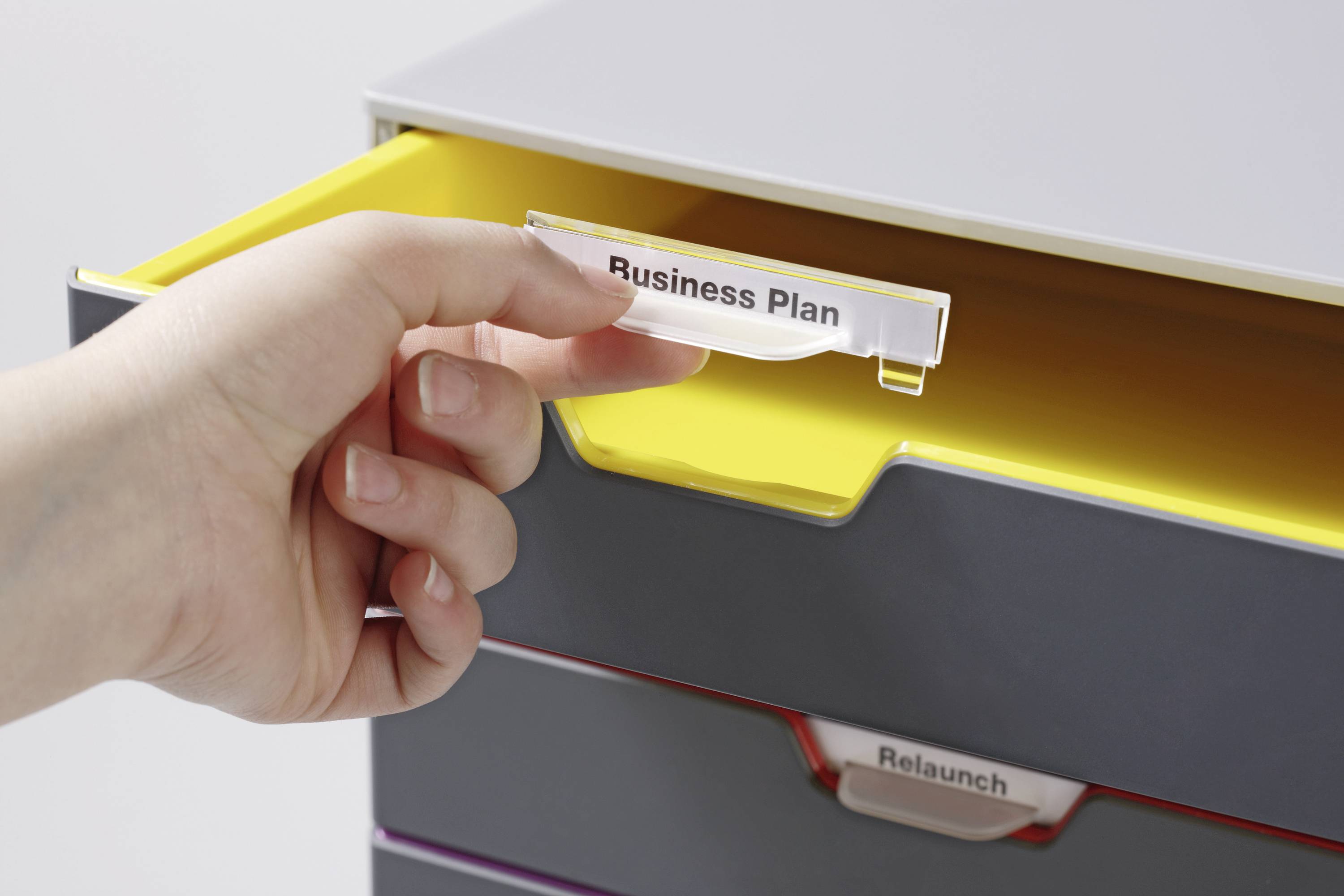Una mano estrae un cassetto con l'etichetta 'Business Plan'. Sotto è visibile un altro cassetto con l'etichetta 'Relaunch'.