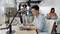 Un uomo concentrato lavora su un laptop in un ufficio open space moderno. Sullo sfondo, colleghi sono riuniti e conversano.