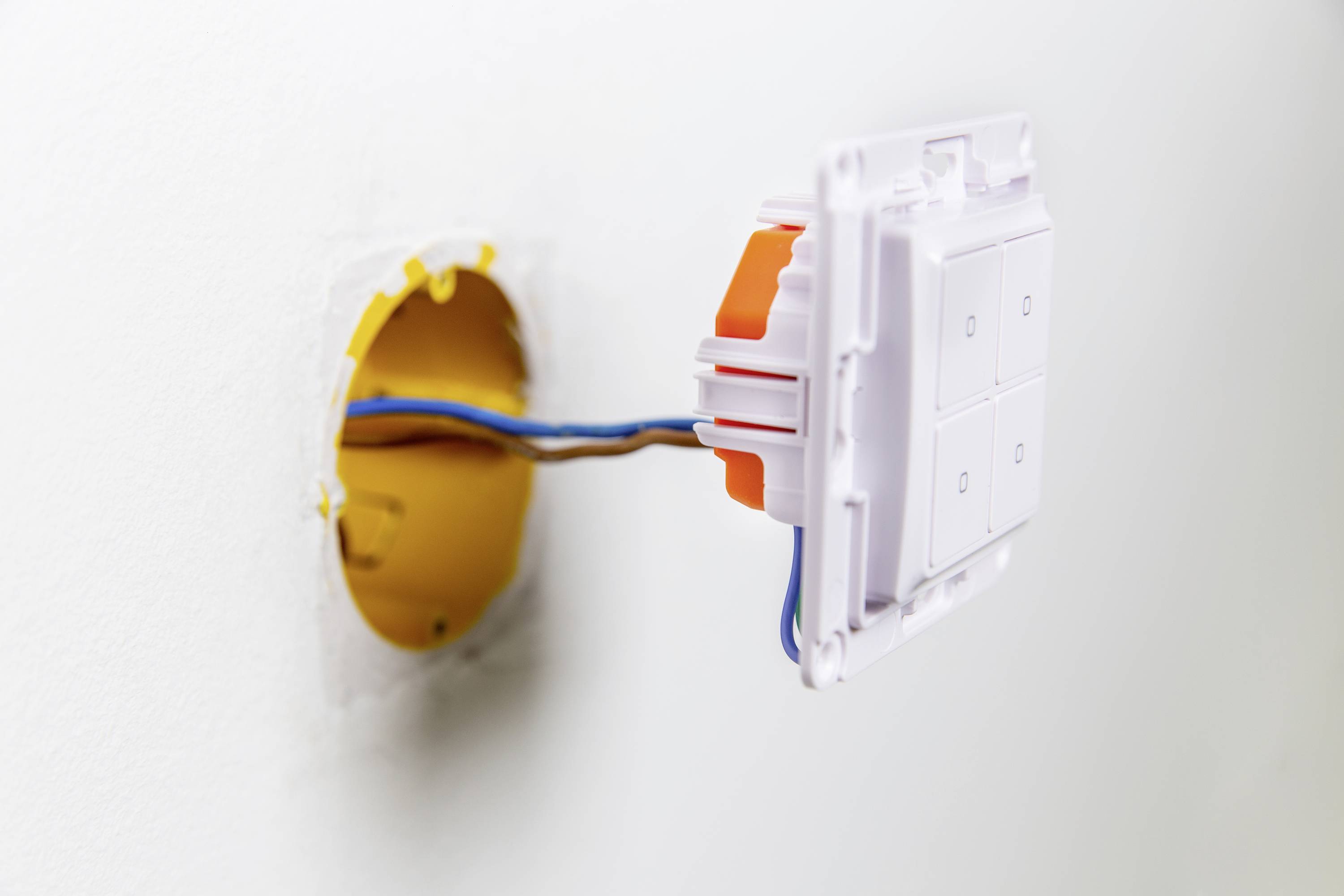 Una presa elettrica aperta a muro con cavi esposti che conducono in un involucro elettronico giallo per cavità.