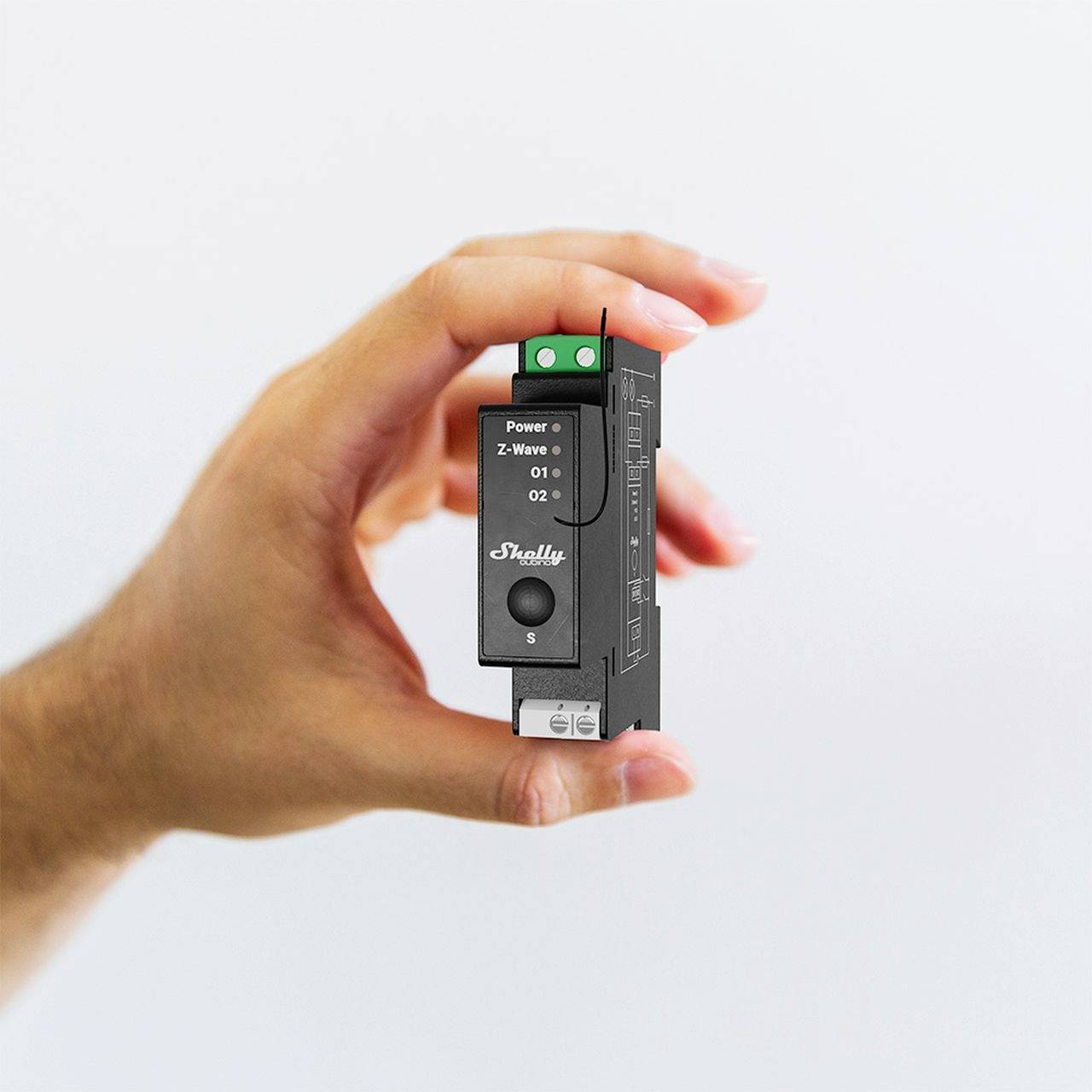 Una mano tiene un piccolo dispositivo elettronico nero con la scritta 'Shelly' e diversi morsetti di connessione e LED.