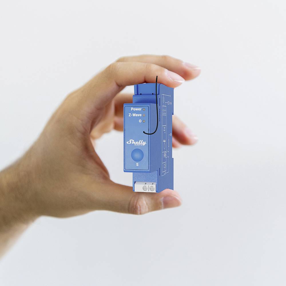 Una mano tiene un interruttore elettrico blu. Sul dispositivo è scritto 'Shelly' e ha LED per 'Power' e 'Z-Wave'.