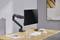 Un tavolo di legno con un monitor nero su un braccio regolabile. Sopra ci sono una tastiera, un mouse, un bicchiere d'acqua e due libri.