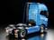 Un camion blu senza rimorchio sullo sfondo scuro, fotografato lateralmente da dietro, con il pianale vuoto e la scritta 'FH16'.