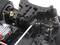 Primo piano di un modellino radiocomandato che mostra il sistema di sospensione anteriore con ammortizzatori, componenti dello sterzo e struttura dei pneumatici.