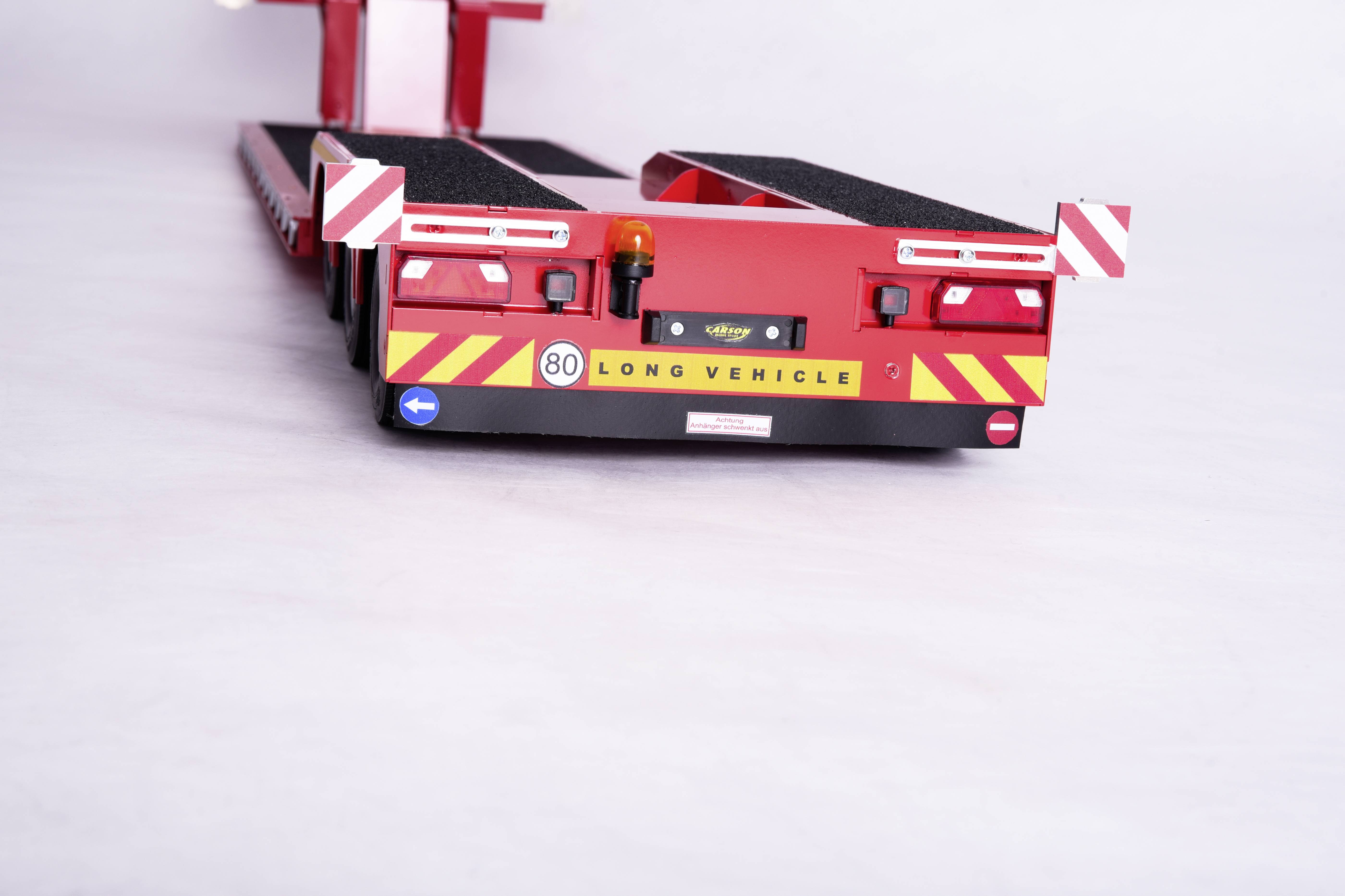 Un rimorchio pesante rosso con segnalazioni "80" e 'LONG VEHICLE' sul retro, mostra marcature di sicurezza e luci posteriori.