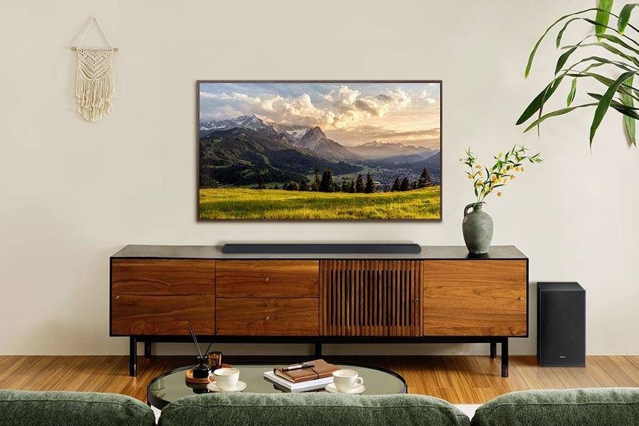 Un soggiorno moderno con un televisore montato a parete che mostra un paesaggio montano. Sotto di esso, un mobile in legno con piante e decorazioni.