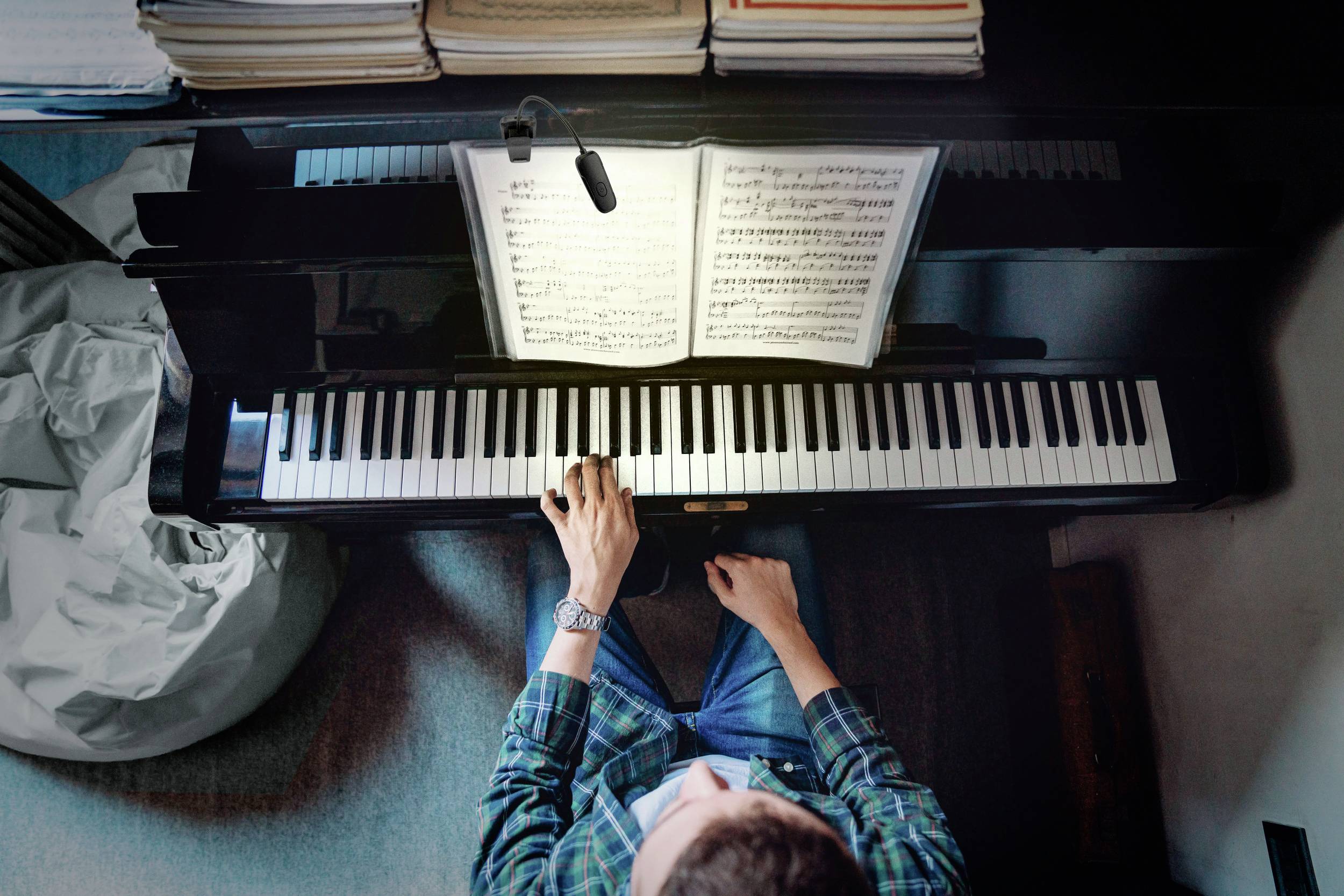 Una persona suona il pianoforte e legge lo spartito posizionato sul leggio. La visuale è dall'alto, con l'attenzione concentrata sulle mani e sui tasti.