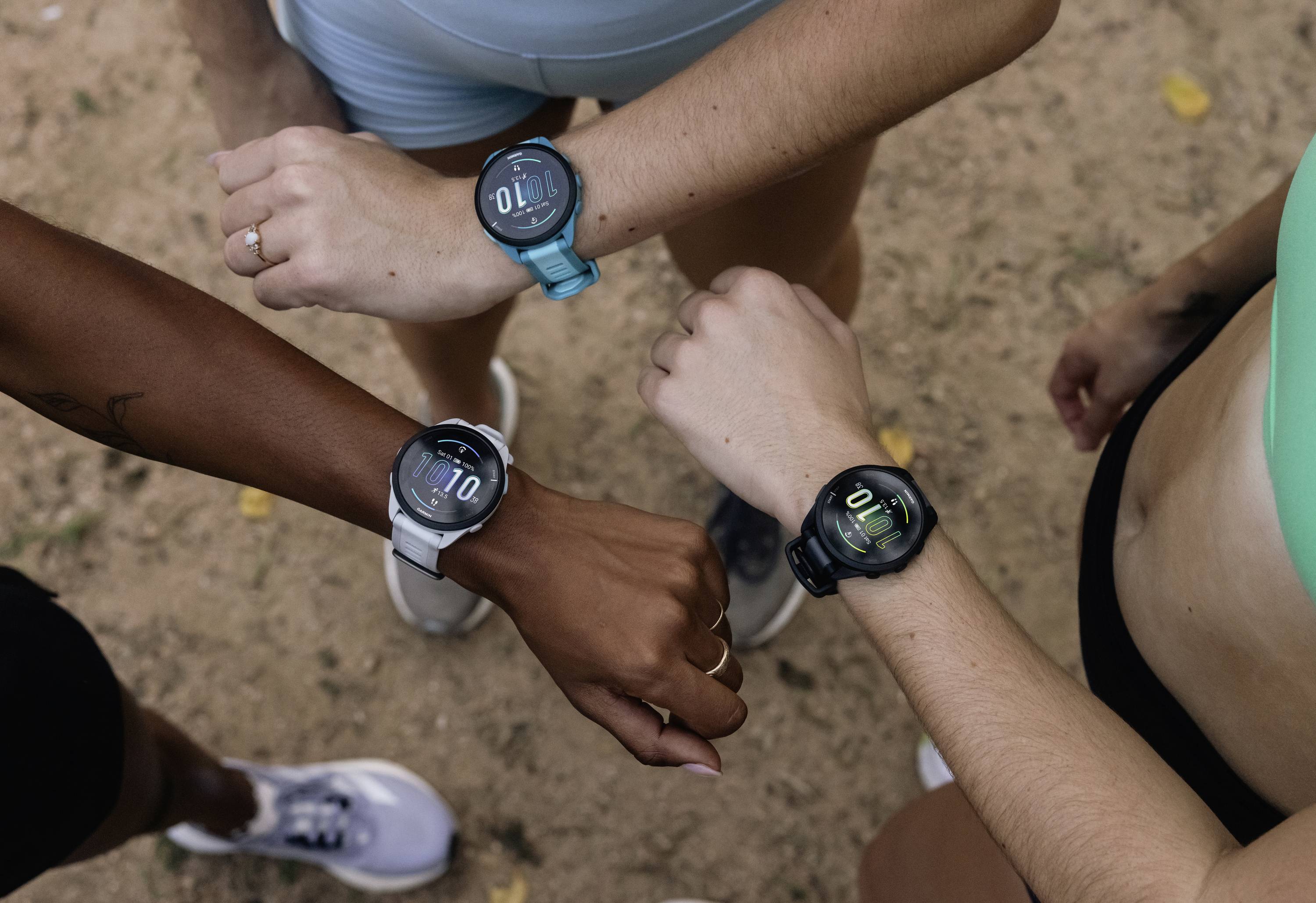 Tre persone sono in piedi insieme e controllano i loro smartwatch fitness. Indossano abbigliamento sportivo e sono su una superficie sabbiosa.