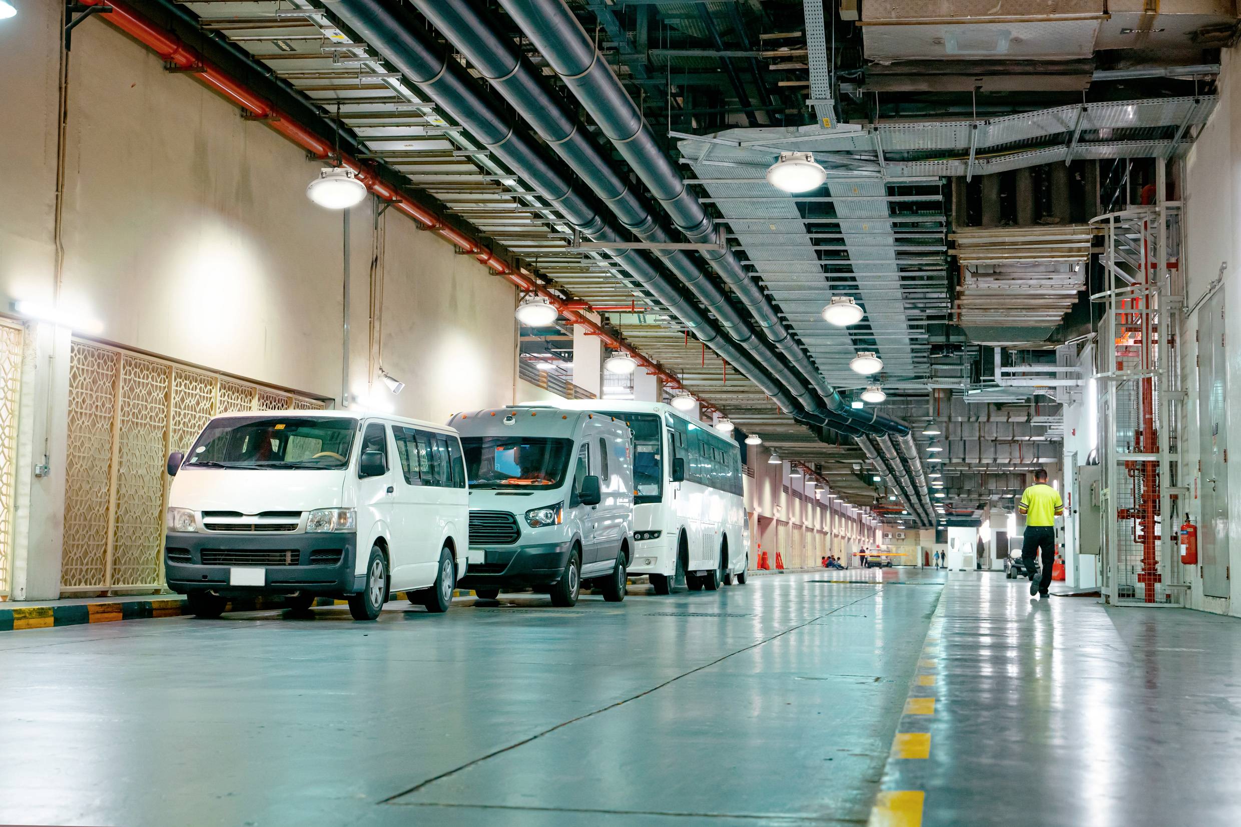 Diversi furgoni bianchi sono parcheggiati in una lunga fila in un garage sotterraneo. Una persona cammina in lontananza.