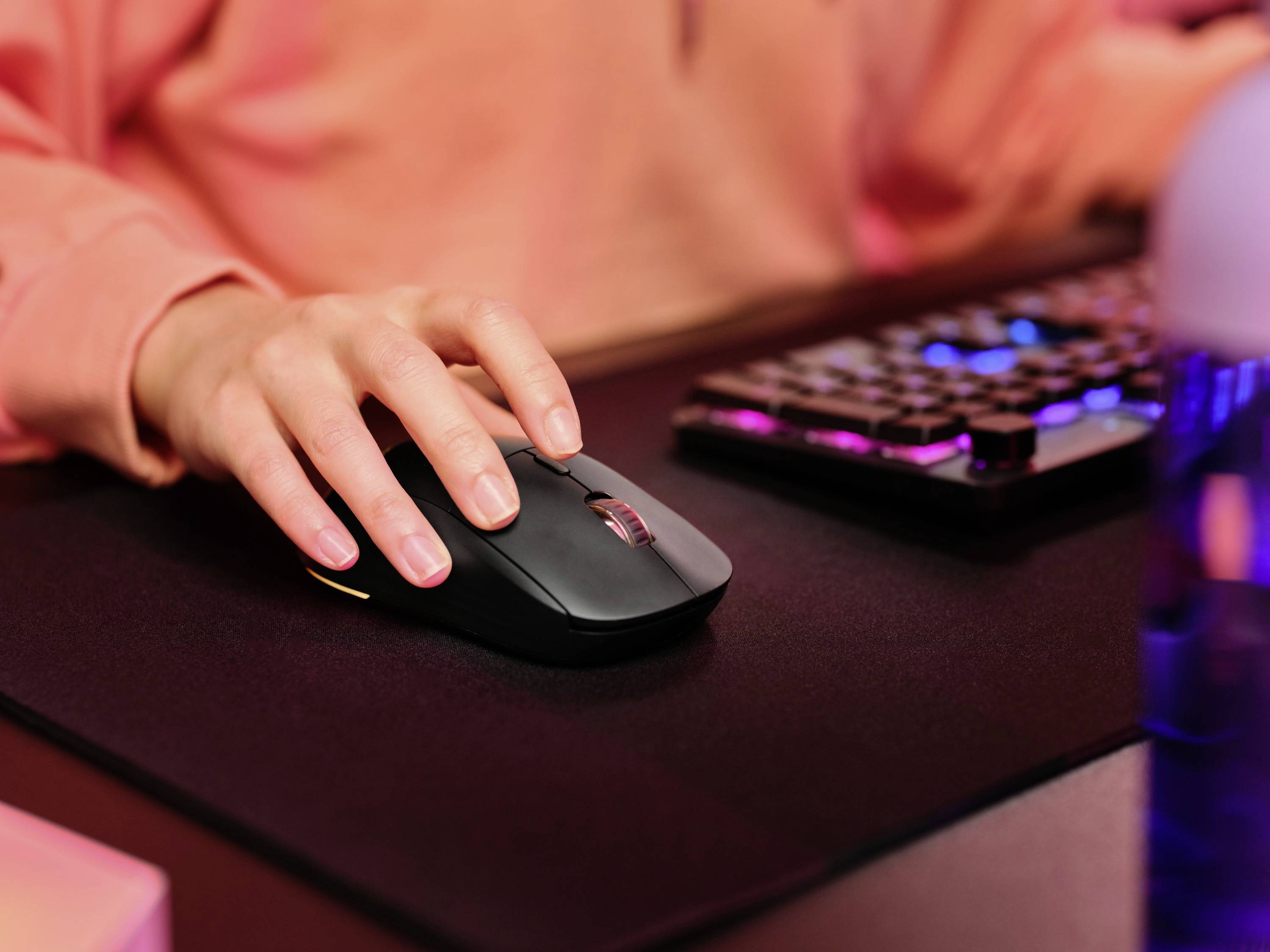 Una persona utilizza un mouse su una scrivania, accanto a una tastiera illuminata.