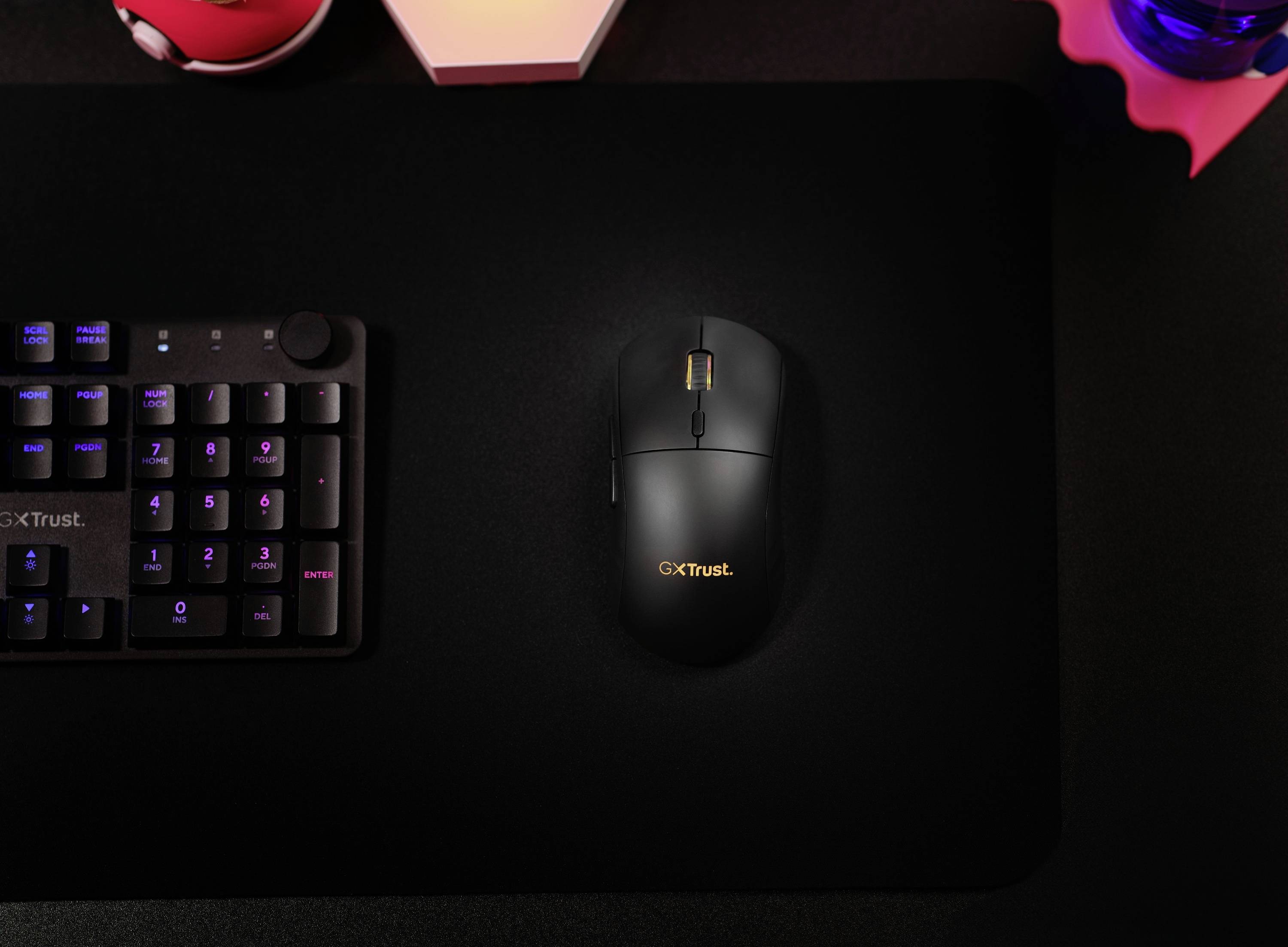Un mouse nero con la scritta 'GxTrust' su un tappetino per mouse scuro, accanto a una tastiera su una scrivania.