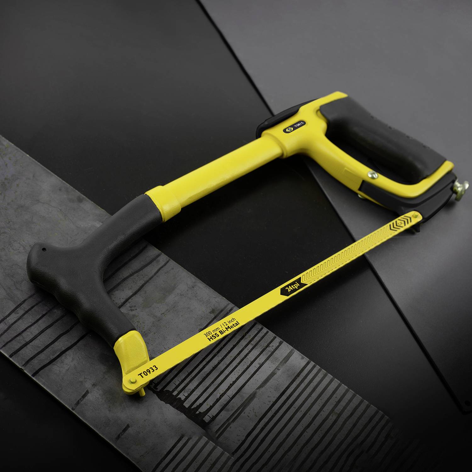 Un seghetto da legno giallo su sfondo nero taglia un nastro nero di gomma o plastica.