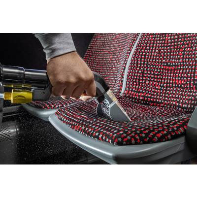 Una persona sta pulendo un sedile a motivi rosso e nero con un aspirapolvere portatile. Goccioline d'acqua spruzzano dall'ugello.
