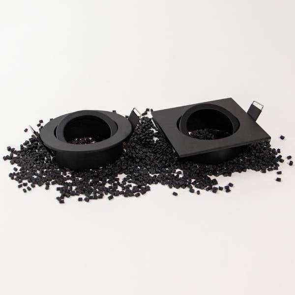 Due portalampade elettronici neri giacciono su un mucchio di piccole graniglie di plastica nera su uno sfondo bianco.