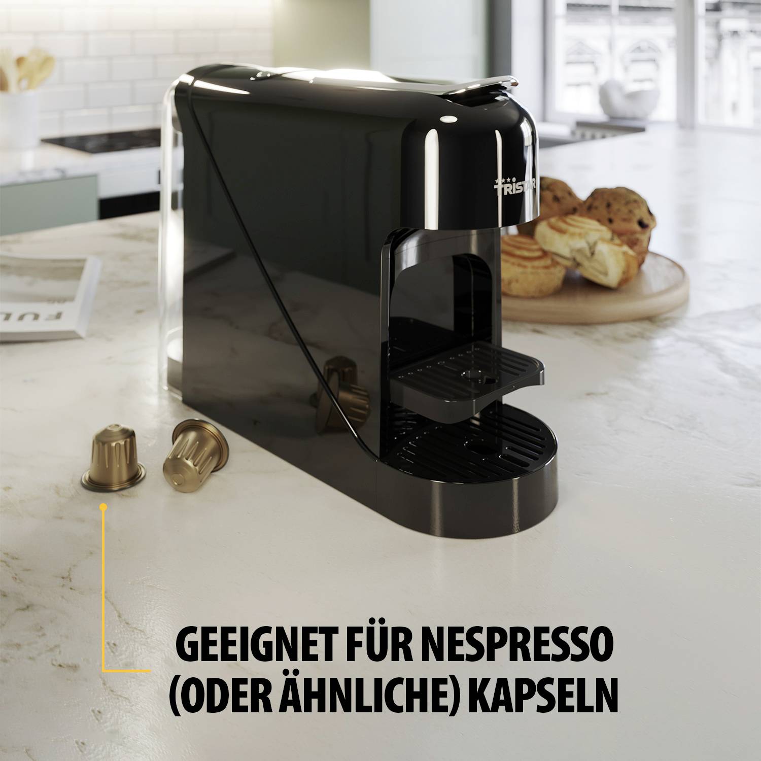 Una macchina per caffè a capsule nera con due capsule accanto. Sullo sfondo, una ciotola con dei croissant. Testo: 'Adatto per capsule Nespresso (o simili)'.
