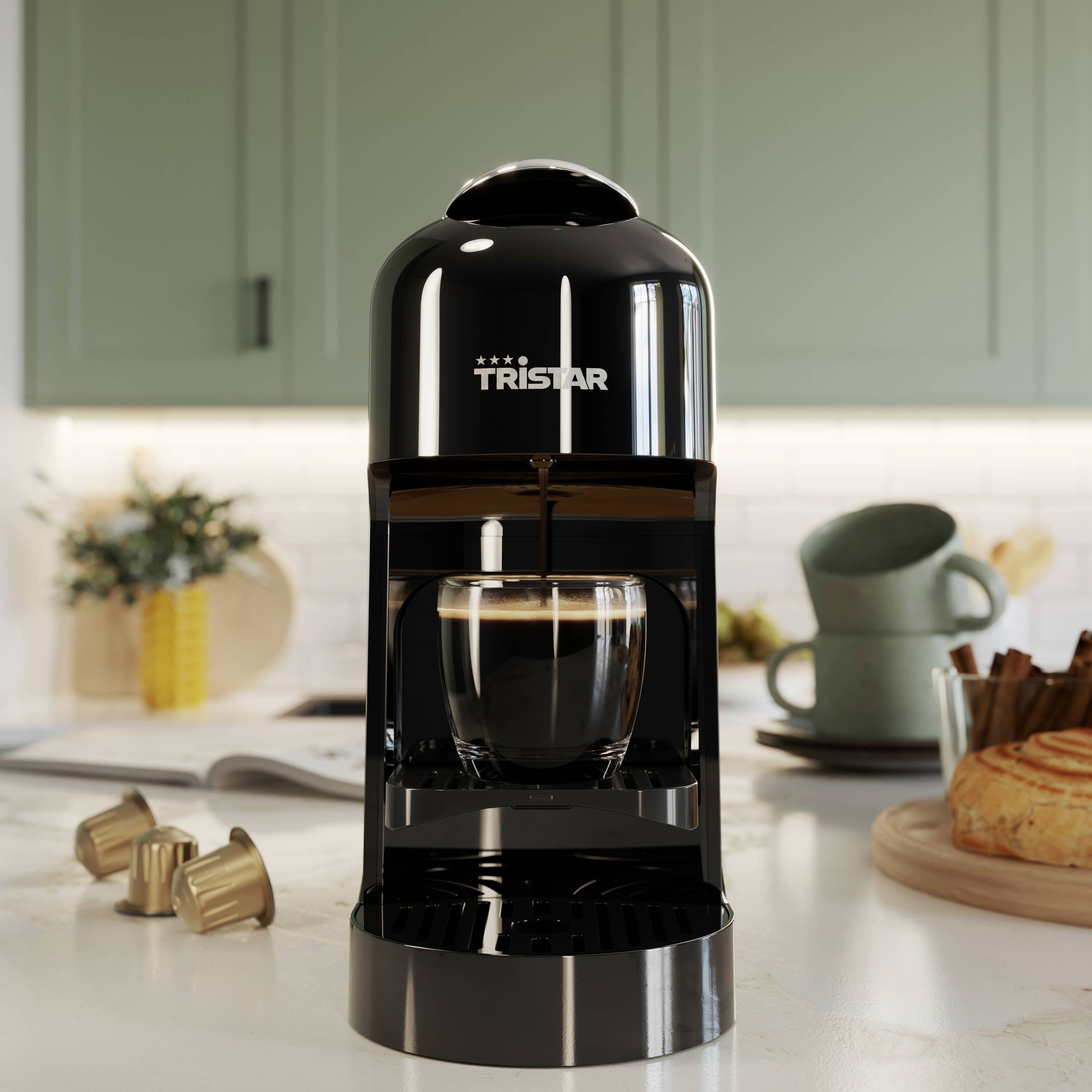 Macchina da caffè in una cucina moderna, con una tazza di espresso sotto. Sullo sfondo, pane e stoviglie sul piano di lavoro.